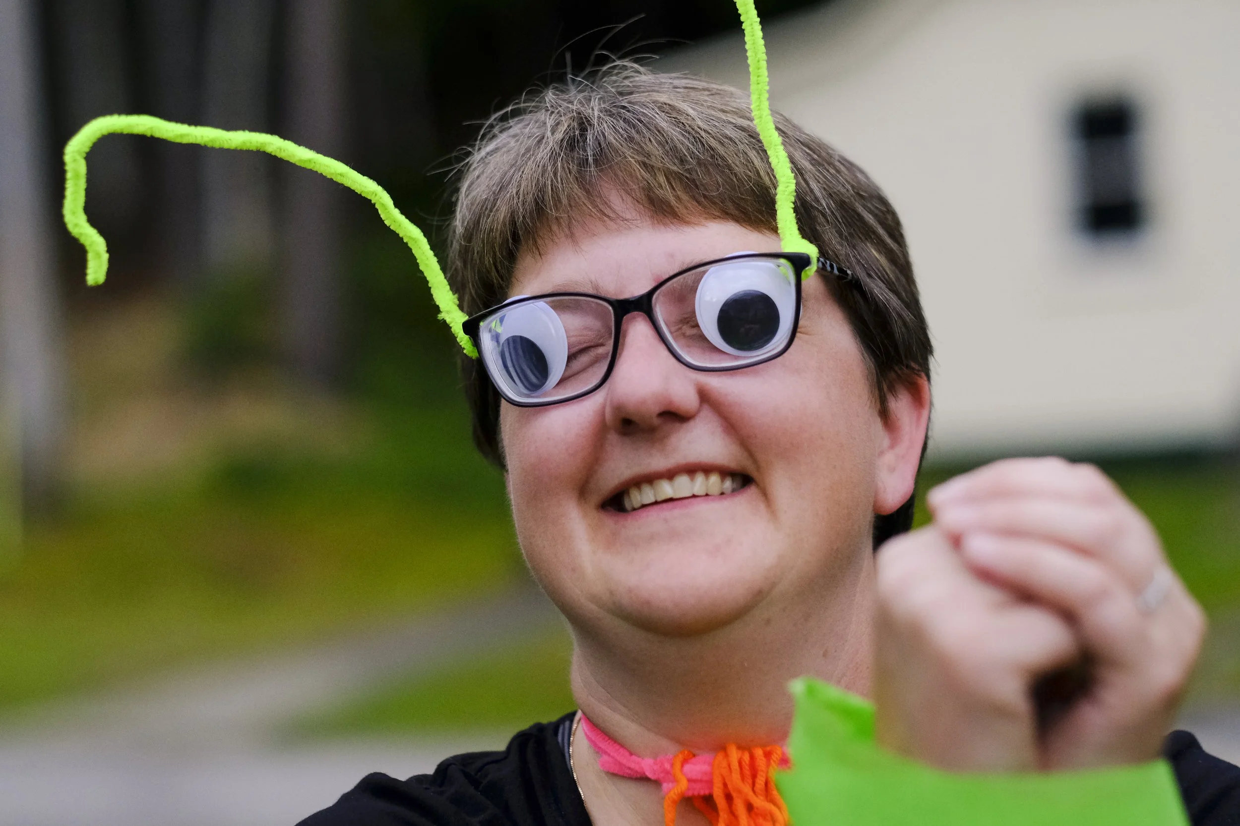 a camper smiles with googly eyes stuck behind glasses and pipe cleaner antenna stick up from the frames; they are channeling their inner fly as part of team building activities