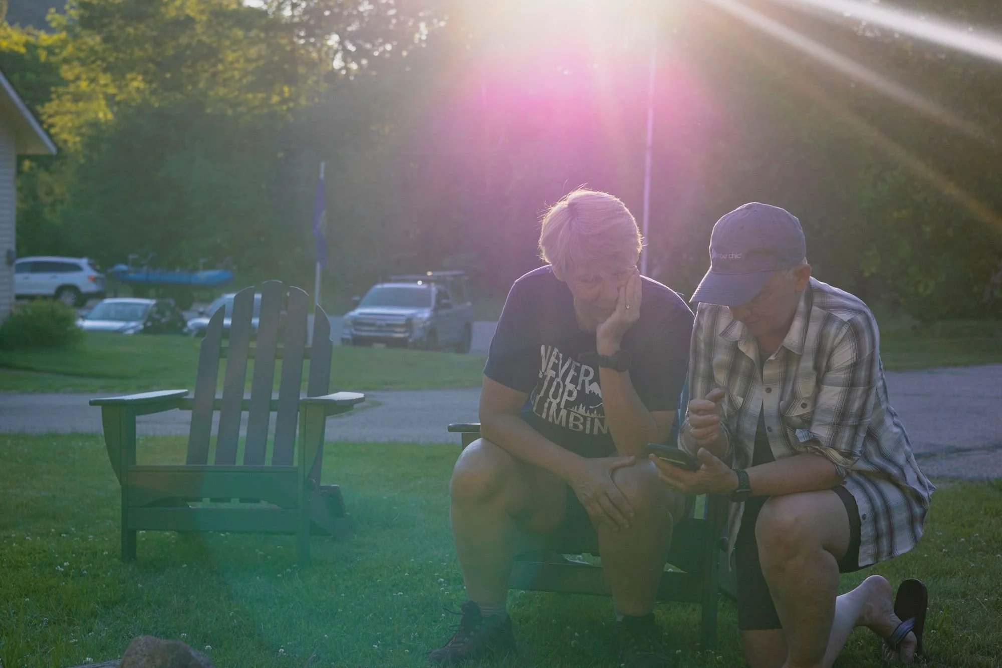 campers sit and kneel together on the lawn in setting sunlight reviewing pictures of fish from the day together