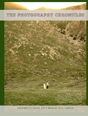 Two people walking on a grassy hillside with rocky terrain under an overcast sky, featured on the cover of The Photography Chronicles magazine.
