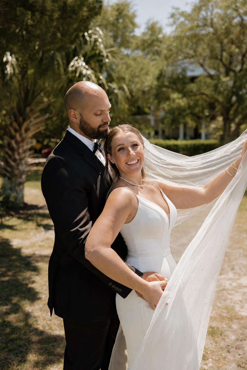 Bride and groom portrait at a waterfront Wilmington wedding near Wrightsville Beach, bride's veil blowing in the breeze under live oaks
