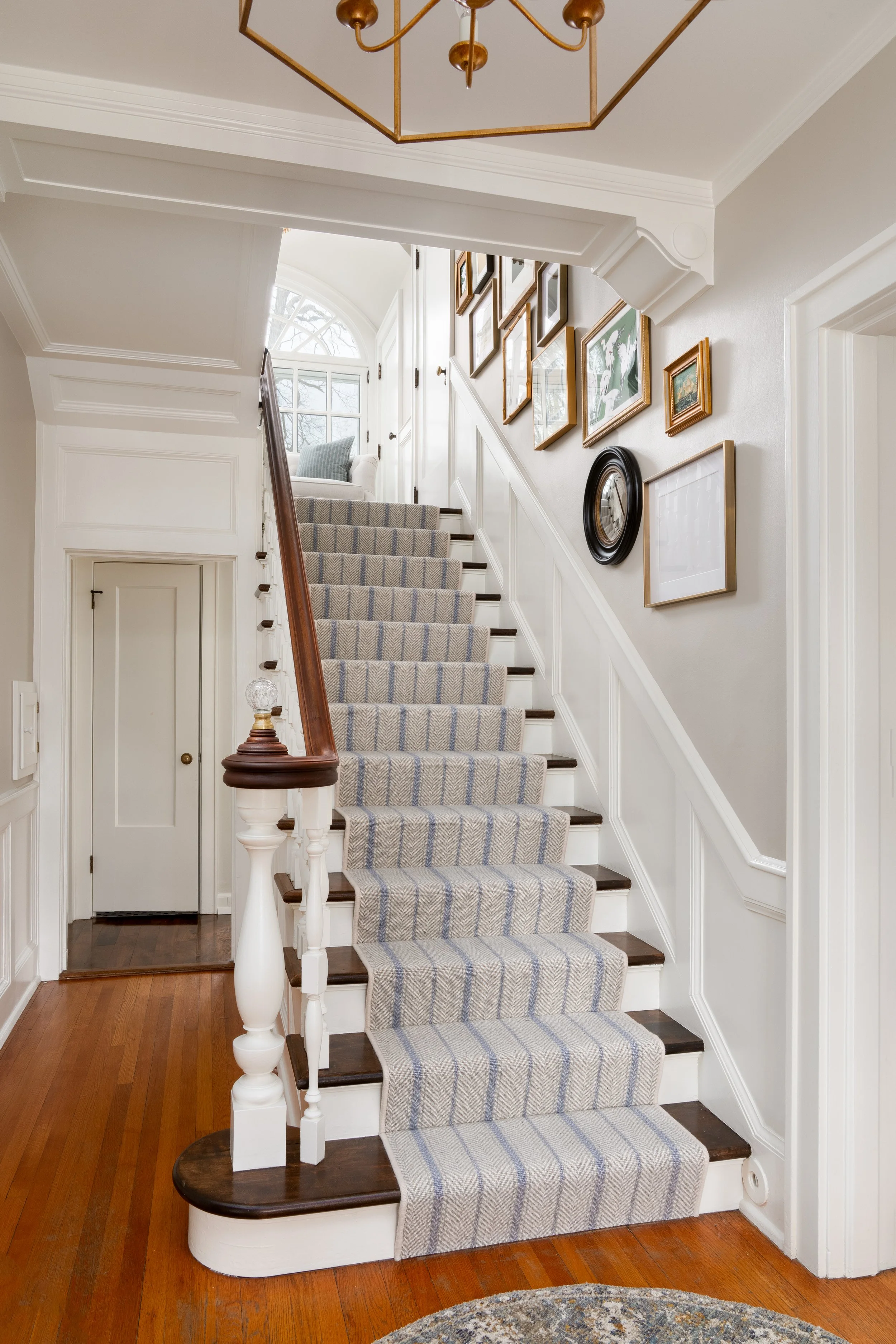 traditional staircase with striped runner, millwork, and gallery wall