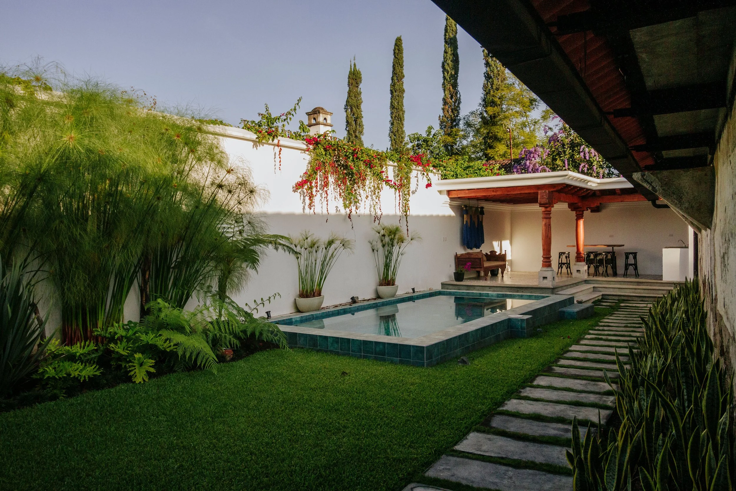 A photo of the spot where we will host the Writers' Workshop. This shows a part of the hacienca with a small pool, green grass, potted plants, and a shaded patio area with outdoor furniture.