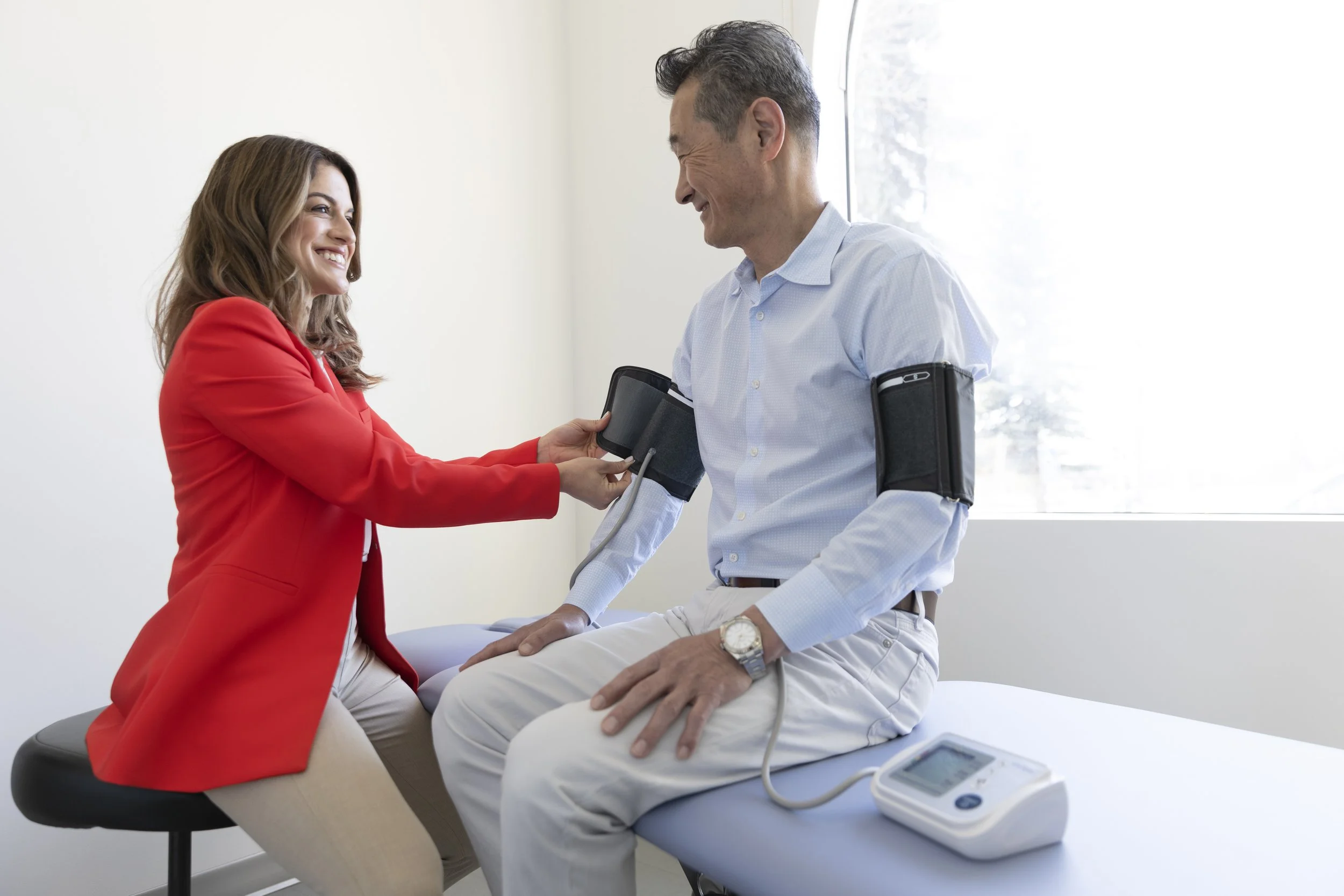 A young female doctor attentively places two blood pressure cuffs on a middle-aged man's arms.