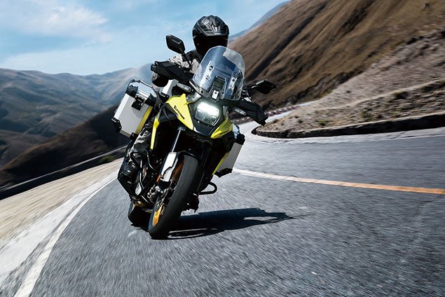 A yellow and black touring motorcycle riding on a winding mountain road with hills in the background.
