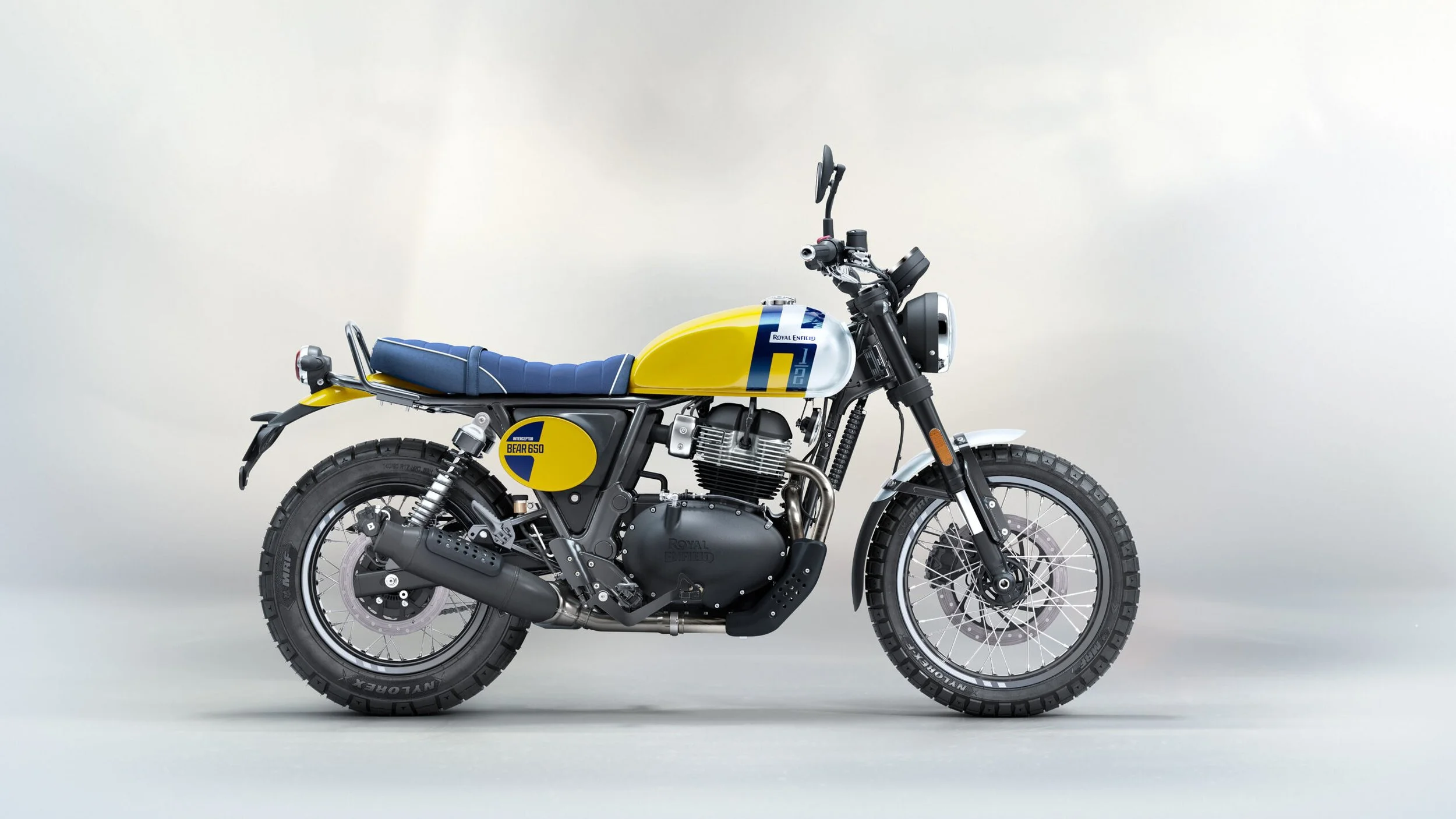 A Royal Enfield Himalayan motorcycle with a blue seat and yellow fuel tank against a plain light background.