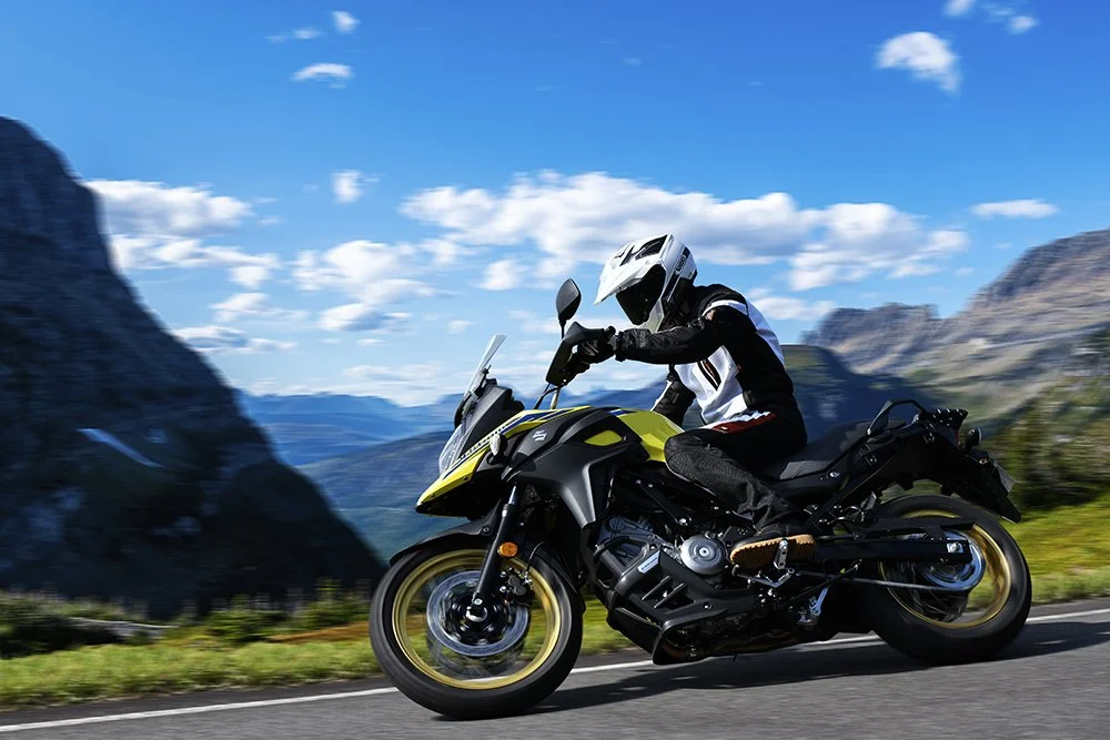 Motorcycle rider in protective gear riding on a mountain road with scenic landscape and blue sky.