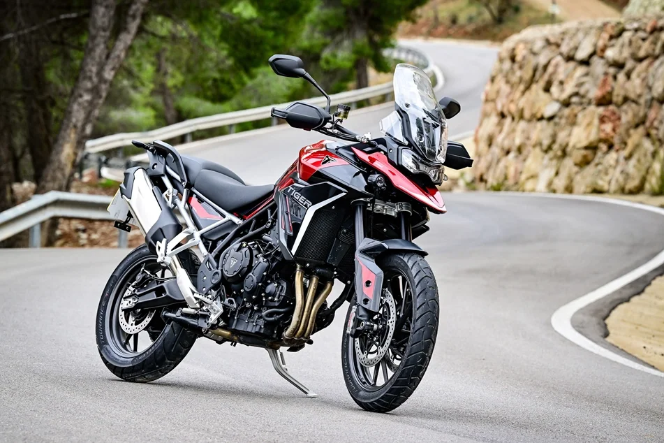 A red and black adventure motorcycle parked on a winding mountain road with guardrails and rocky terrain.