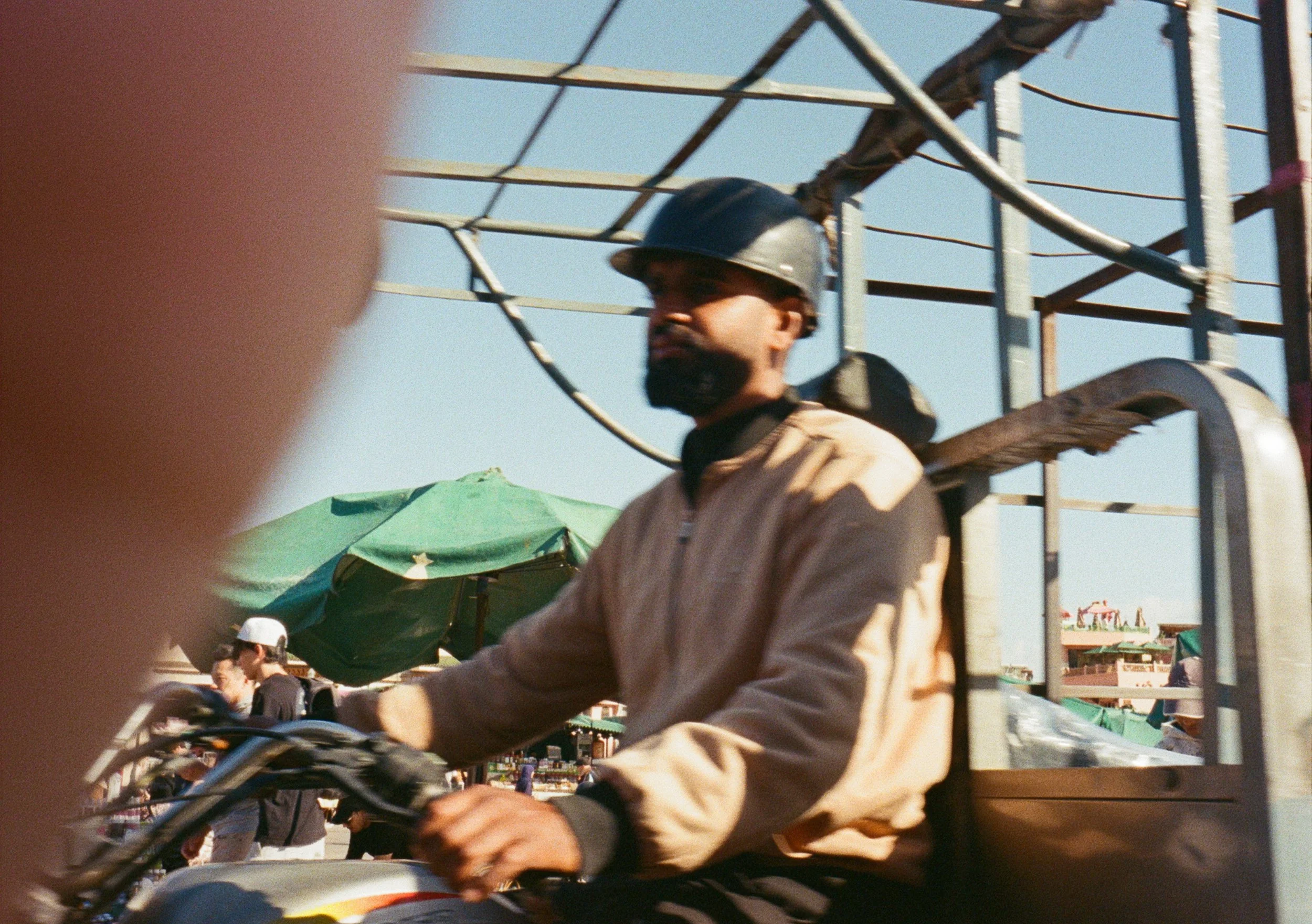 A person wearing a helmet riding a bicycle at an outdoor market with umbrellas and other people visible in the background.