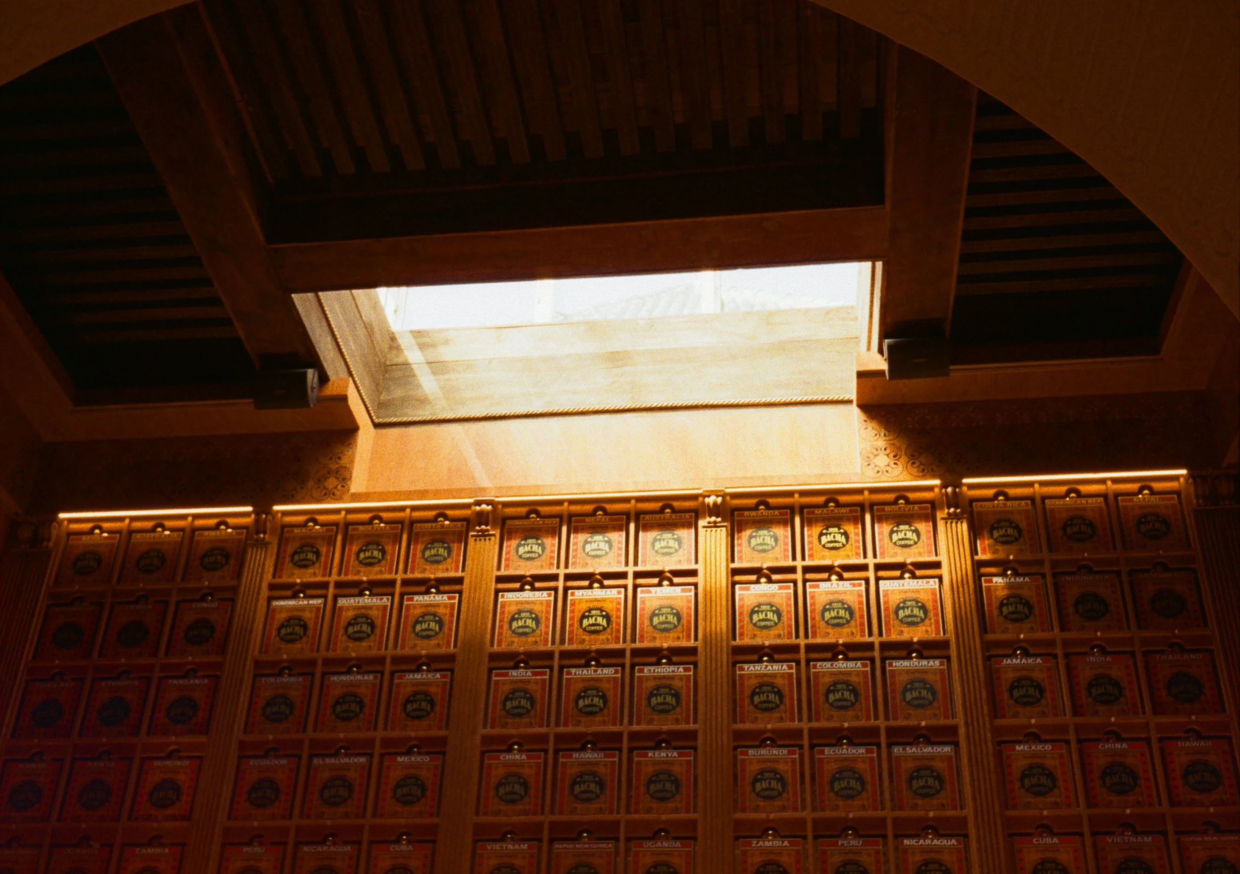 Indoor shot of a wooden ceiling with a rectangular skylight letting in natural light. Below, there is a wall filled with framed labels of various countries.