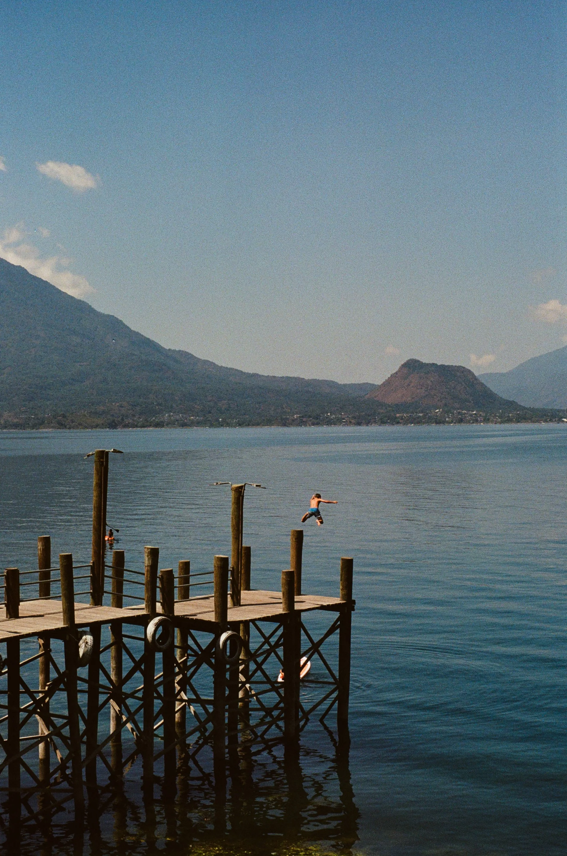 A wooden dock over water with children playing, mountains in the background, and a clear sky.
