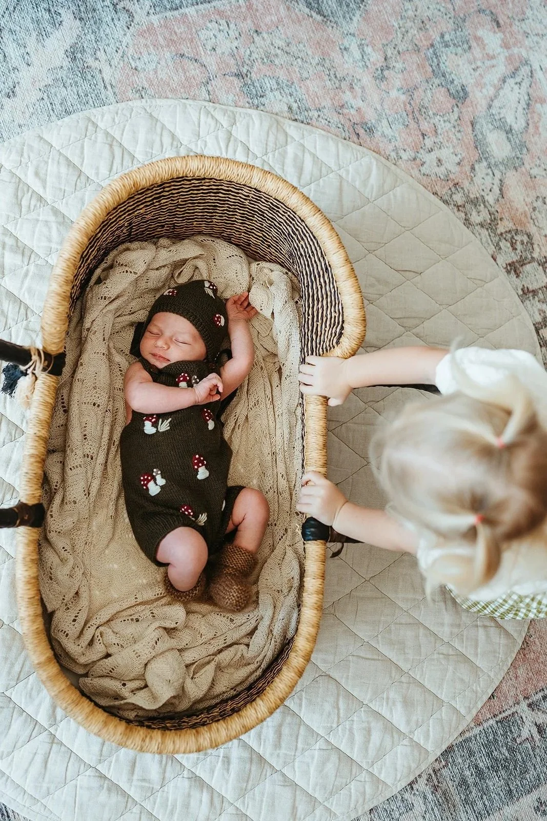 a toddler peeking into a basket at her little newborn sister during a newborn photography session