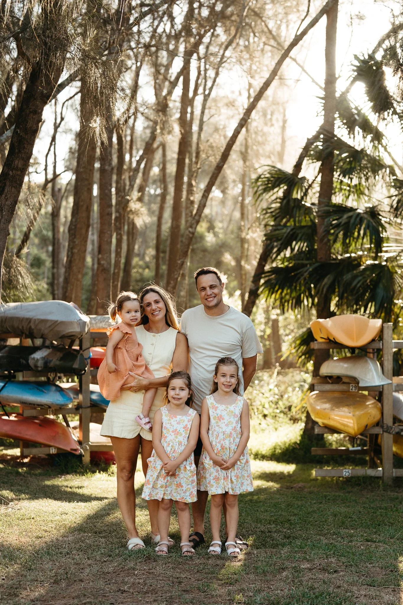 A family having their photo taken at sunset golden hour by Narrabeen Lake, with colourful boats in the background, during a family photography session with Sophie Smith in Sydney.