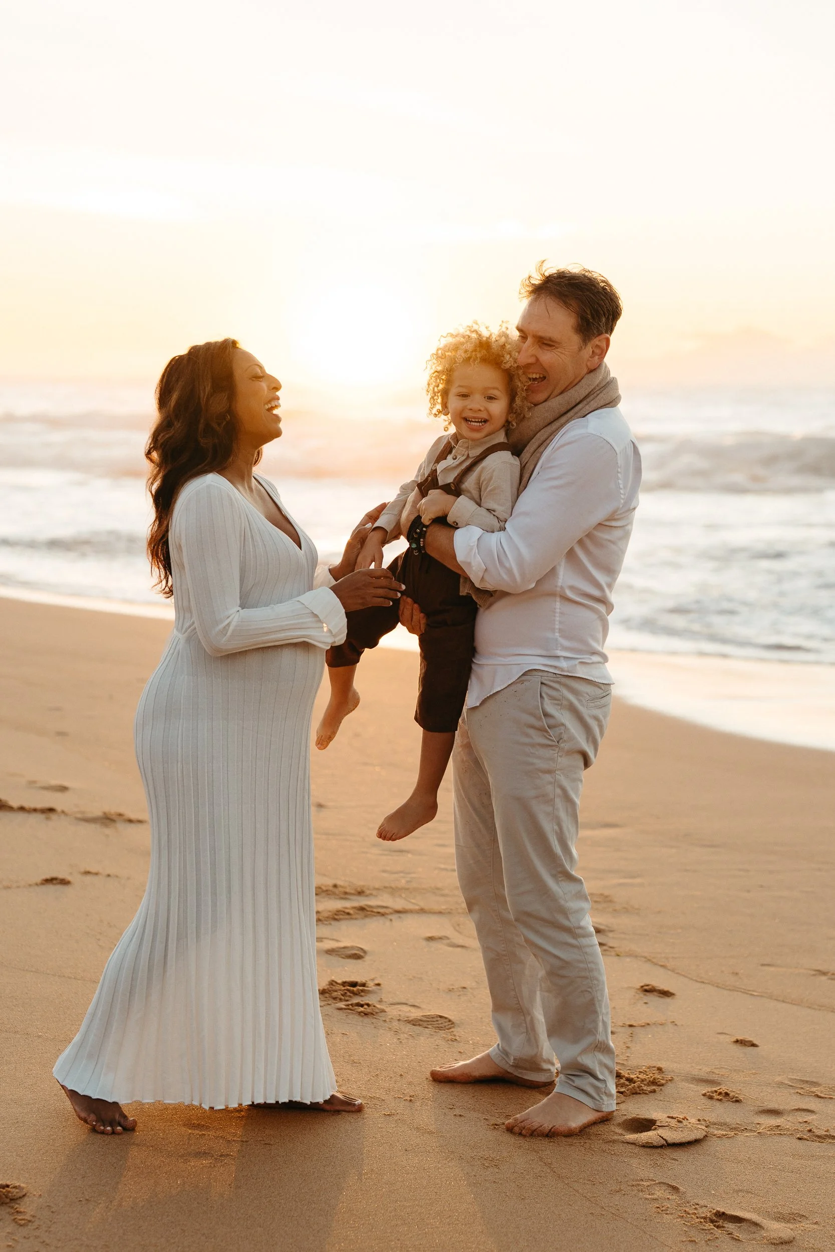 A family with one child laughing on the beach during a family photography session in Sydney