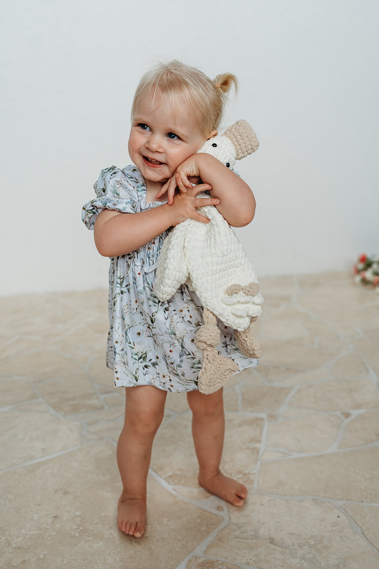 photo of a little girl holding a soft toy and smiling while at a brand photography session for a clothing brand