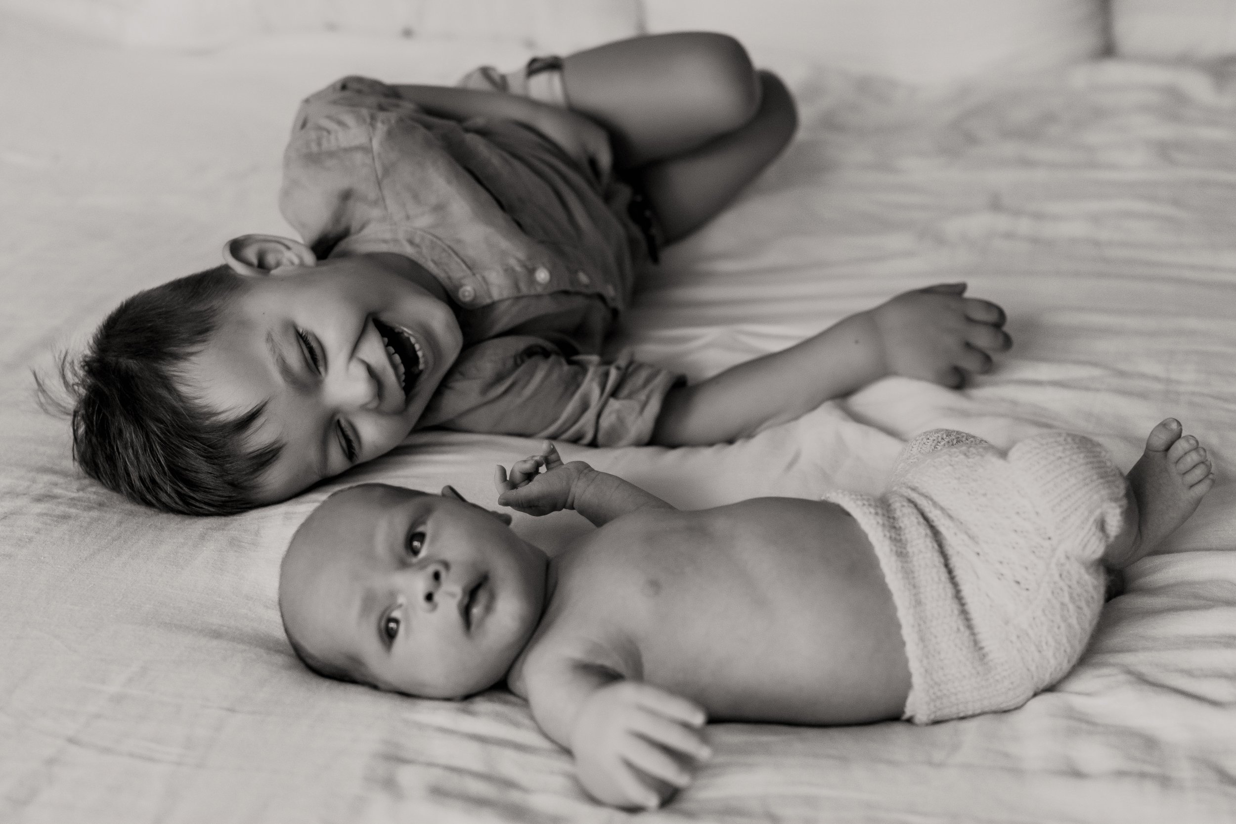 Toddler and his baby brother having their photo taken on the bed at home