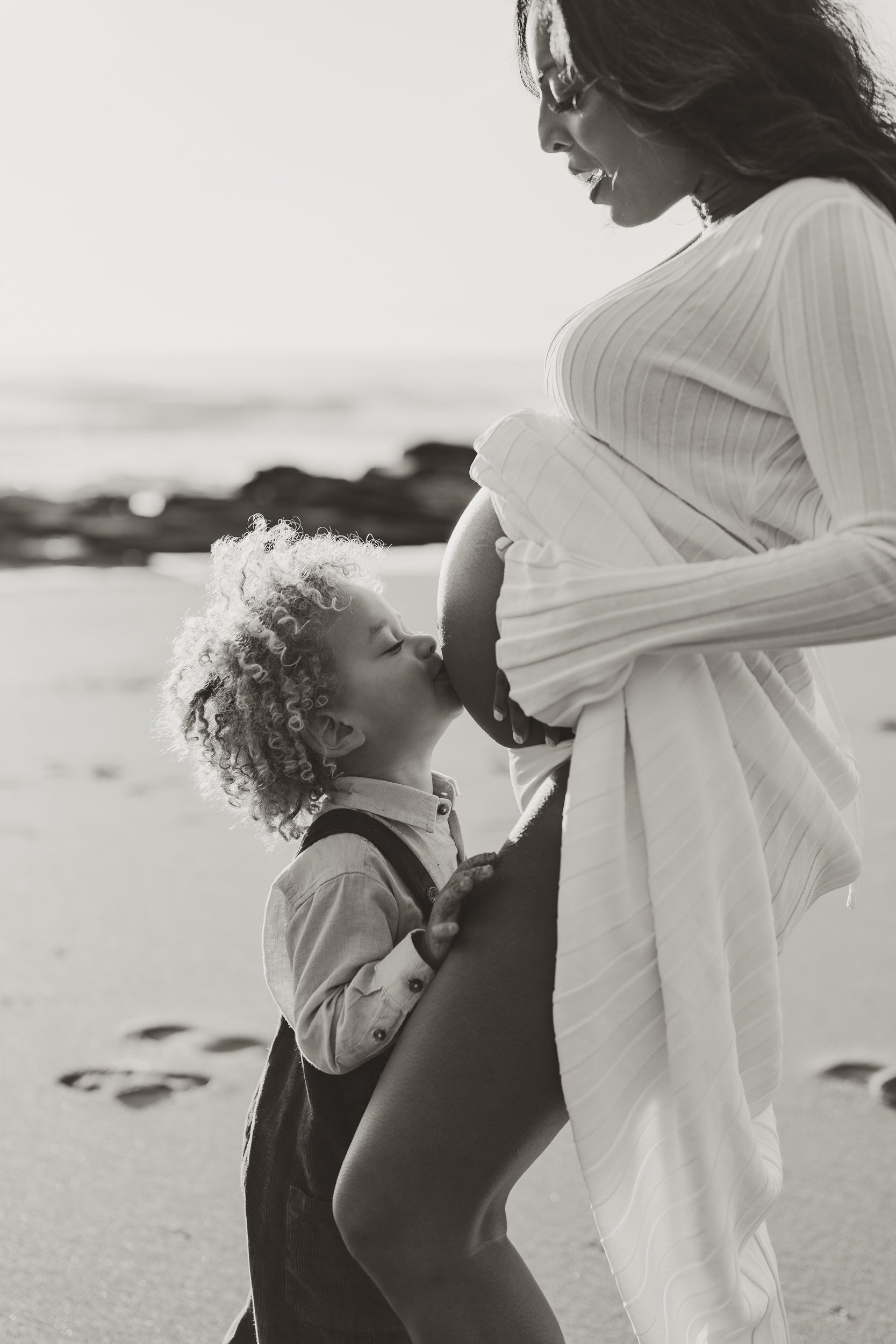 Little boy kissing his Mum's pregnant belly during a beach photography session in Sydney
