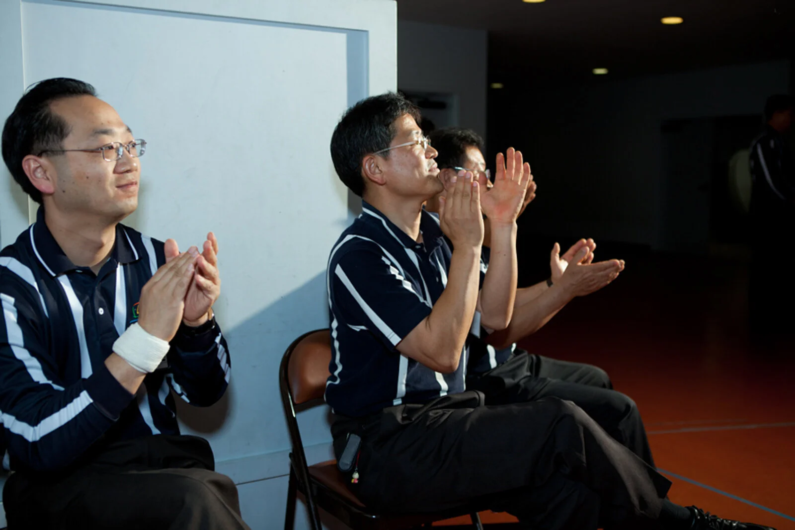 A group of men wearing black and white striped shirts clapping and watching an event.