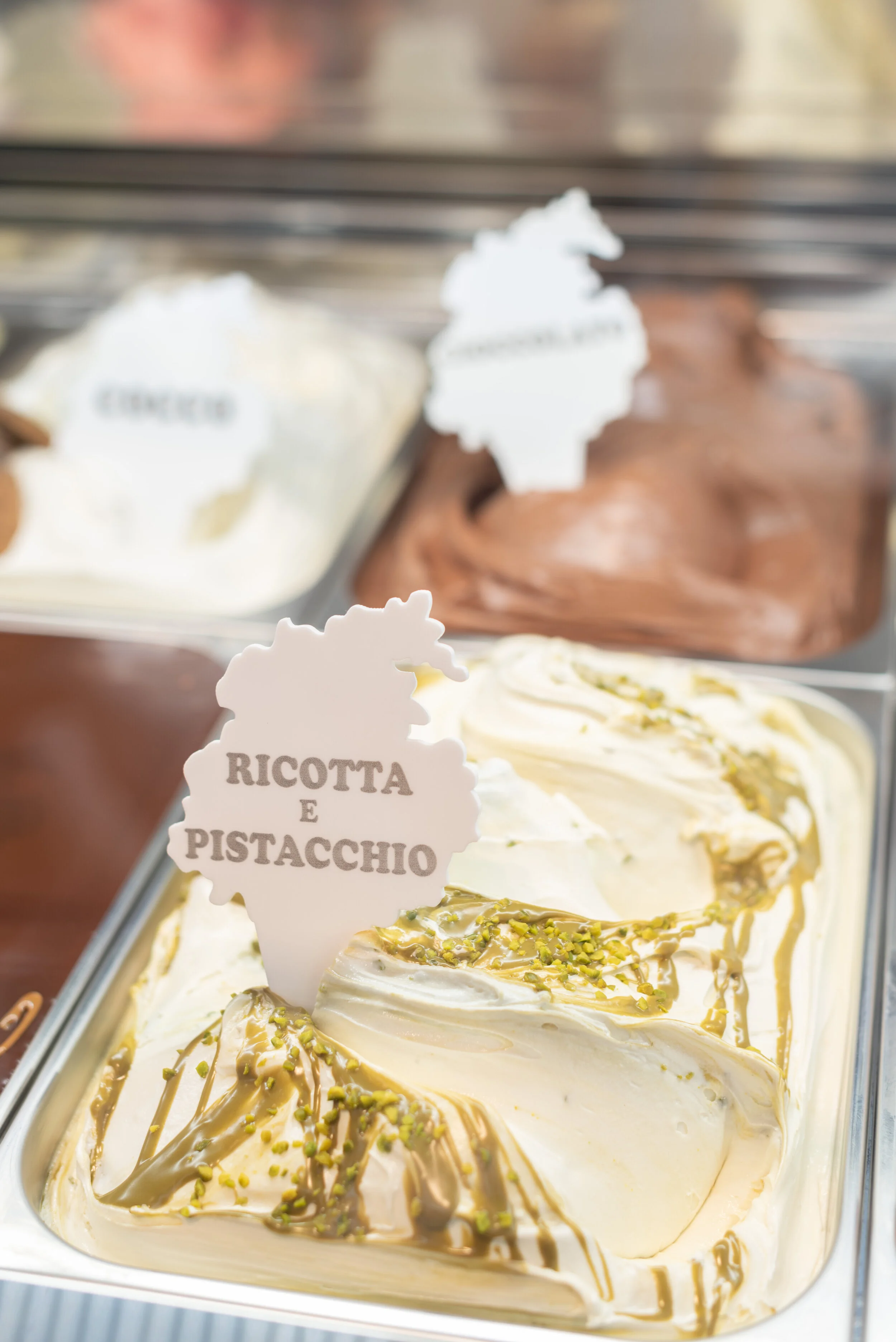 Verschiedene Eissorten in einer Eisdiele, darunter Ricotta und Pistazien mit Pistazienstücken und Erdnußöl