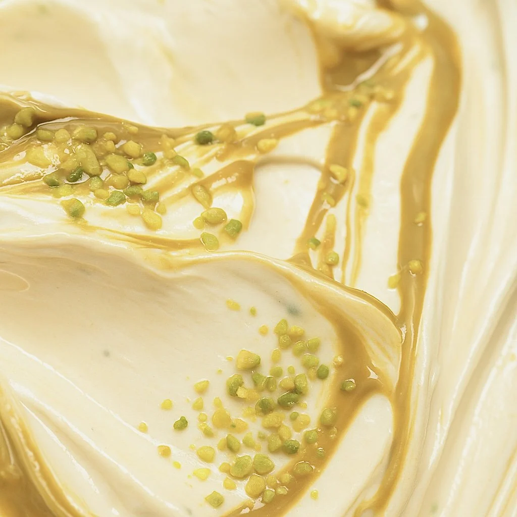 Nahaufnahme von cremiger weißen Schokoladen- oder Vanille-Eisschicht mit grünen Pistazienstückchen und Schokoladenswirl
