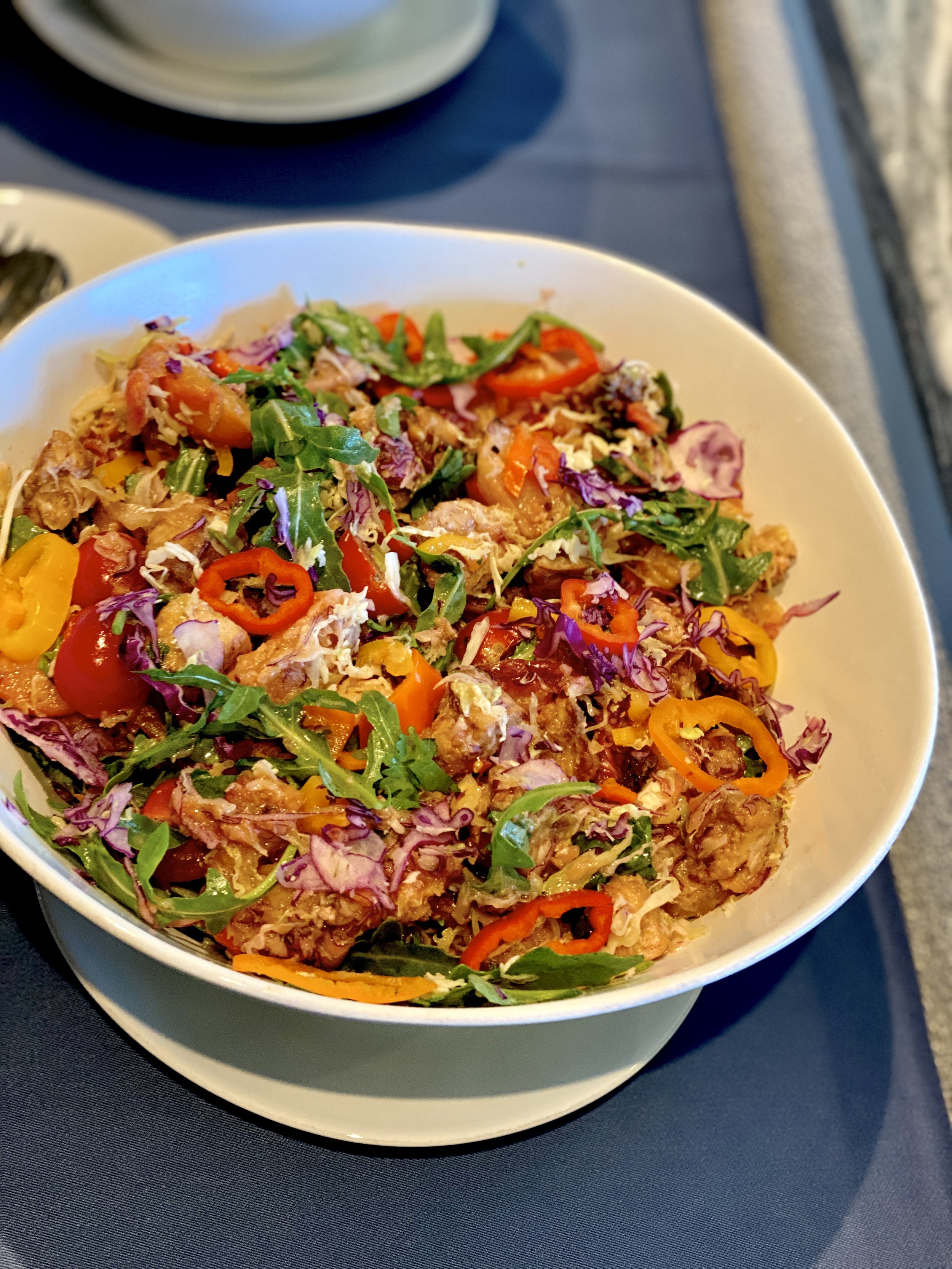 Colorful salad with mixed greens, cherry tomatoes, sliced red peppers, shredded purple cabbage, and crispy fried chicken pieces in a white bowl.