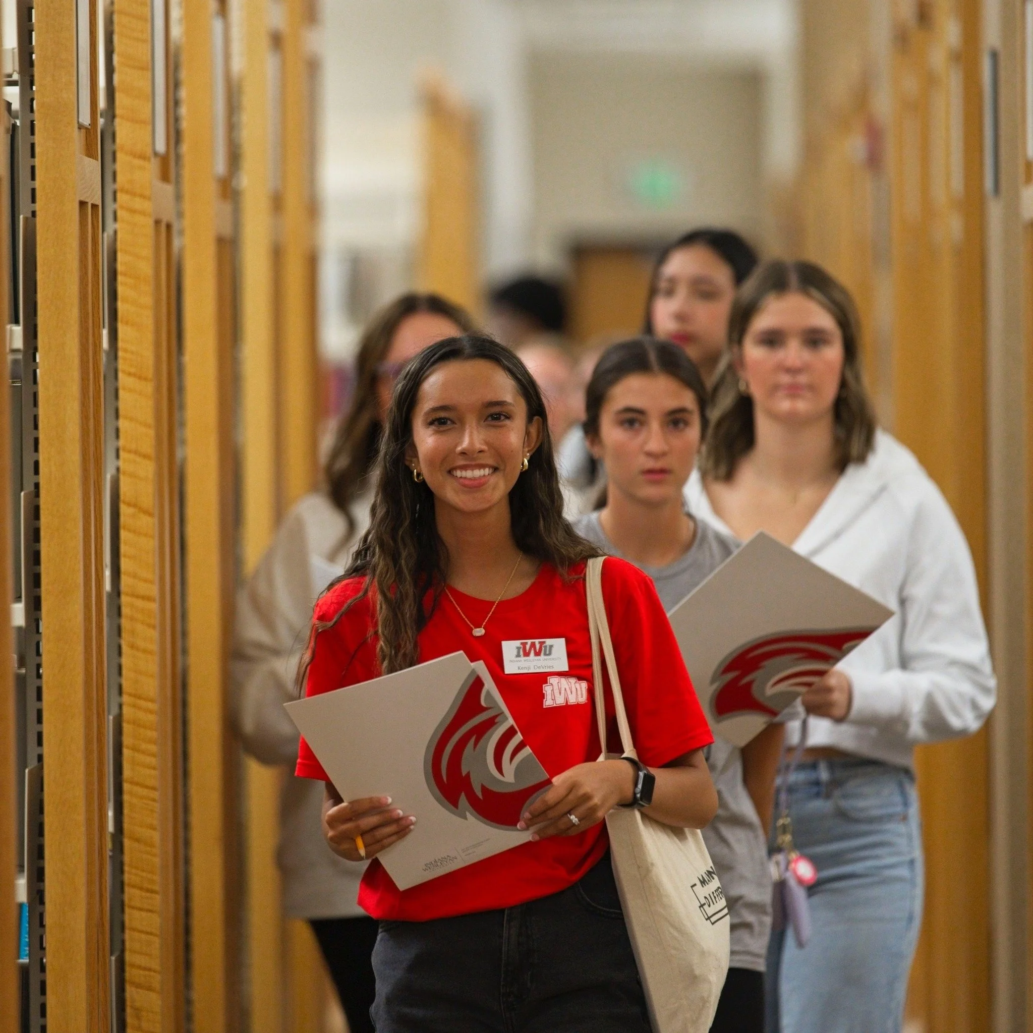 Two young women wearing red Wildcats shirts walking at outdoor event with red tents and people in background.