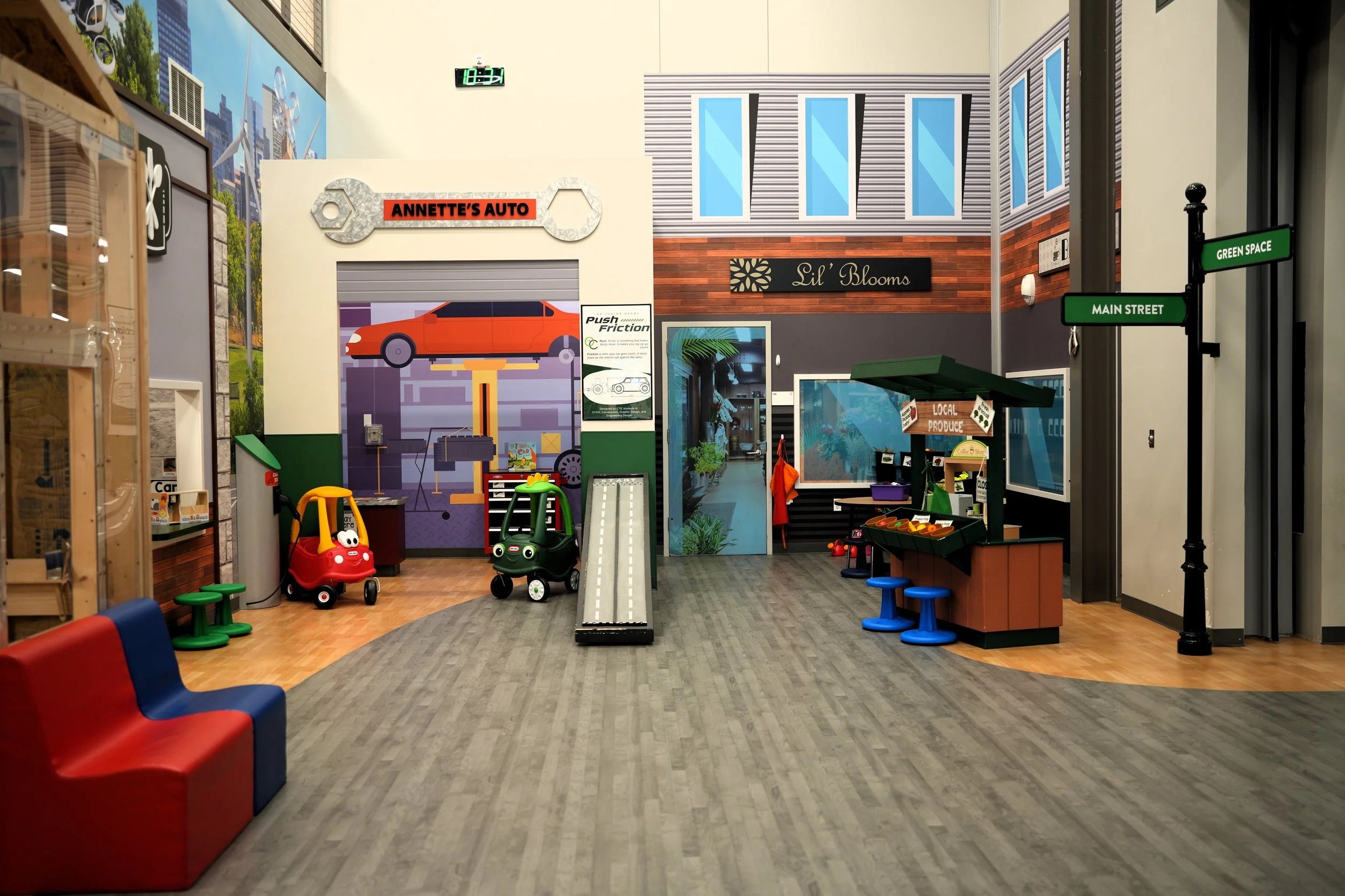 Indoor play area with toys, seating, colorful signs, and a faux storefront for a children's shopping or market area.