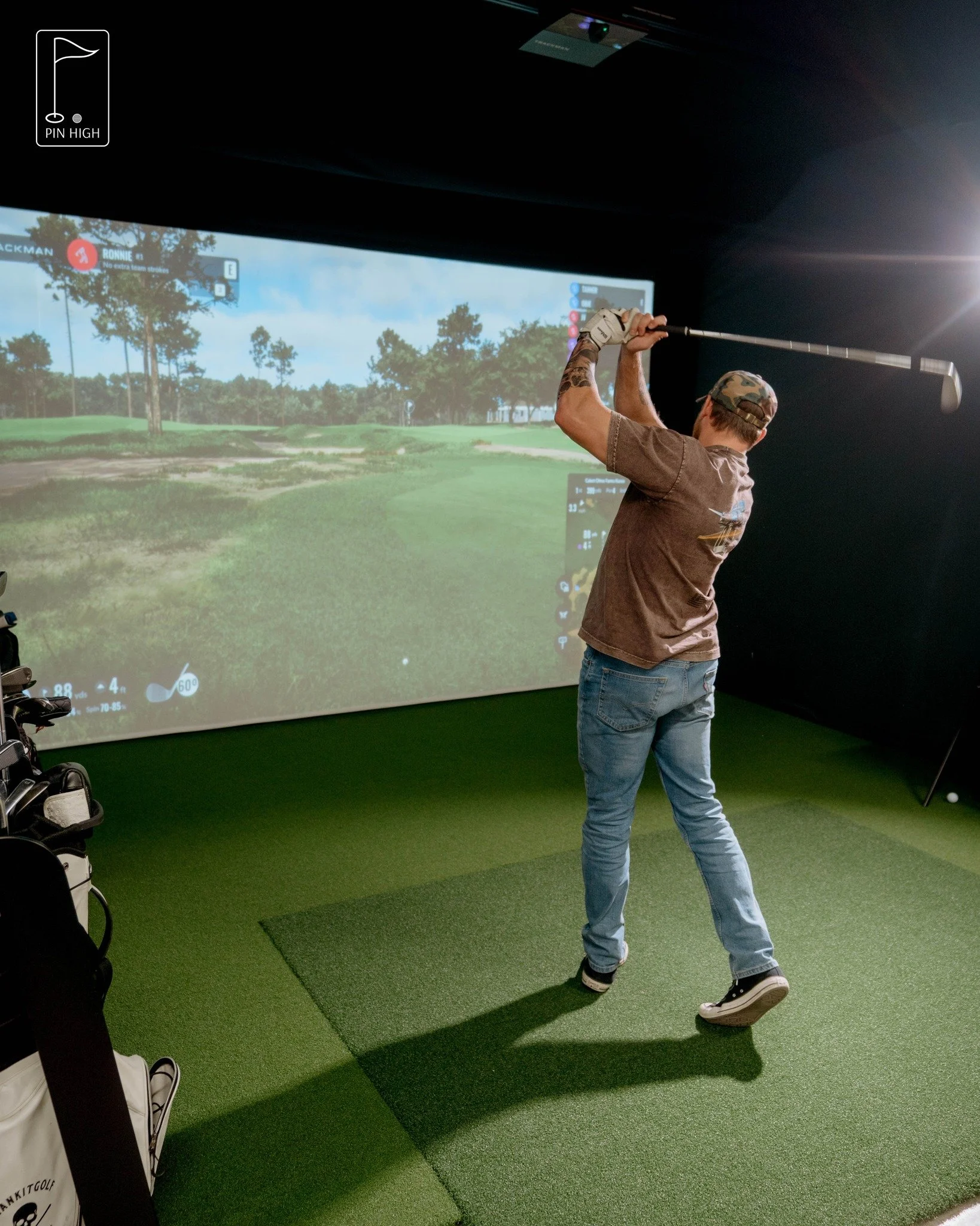Man practicing golf swing in indoor golf simulator with a large screen displaying a golf course.