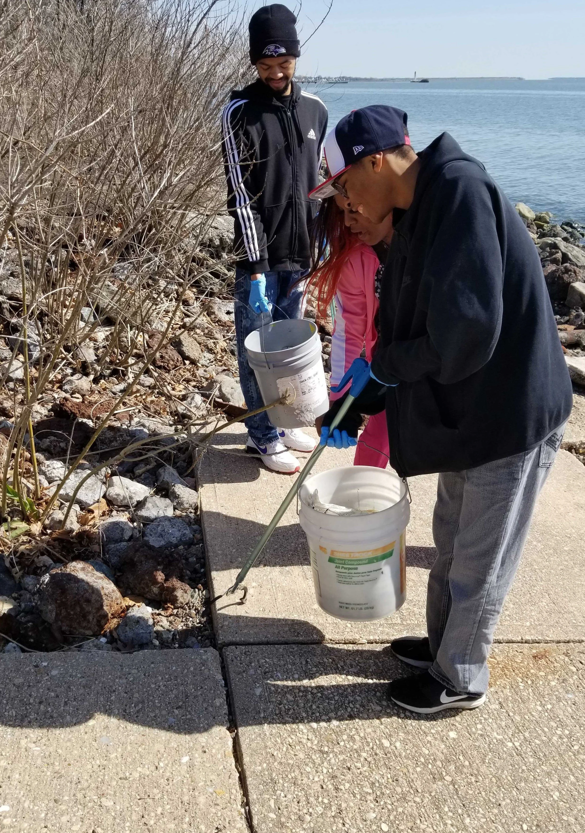 man in black sweatshirt picking up trash on sidewalk