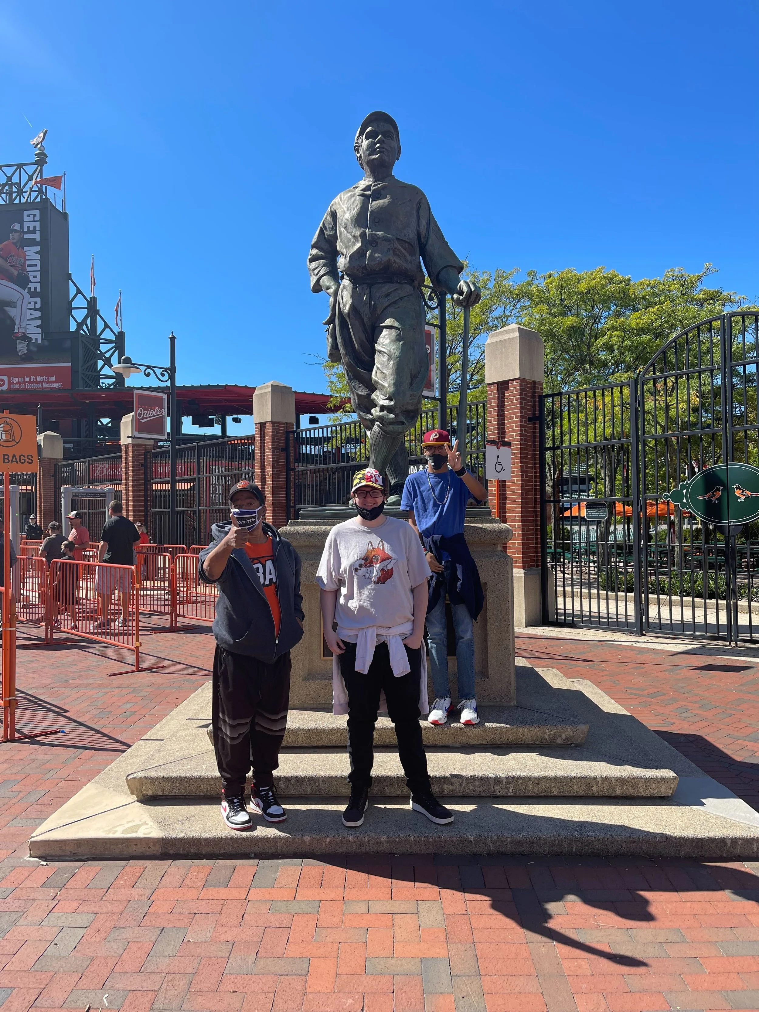 three people posing in front of statue at baseball stadium