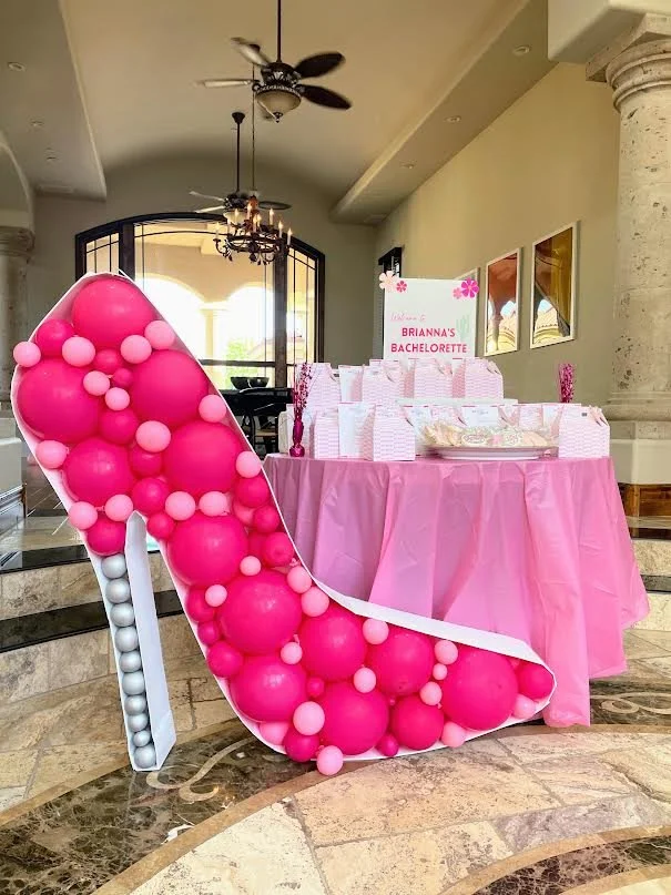 Bachelorette party decoration with a pink high heel balloon sculpture and a table with pink tablecloth and party favors.