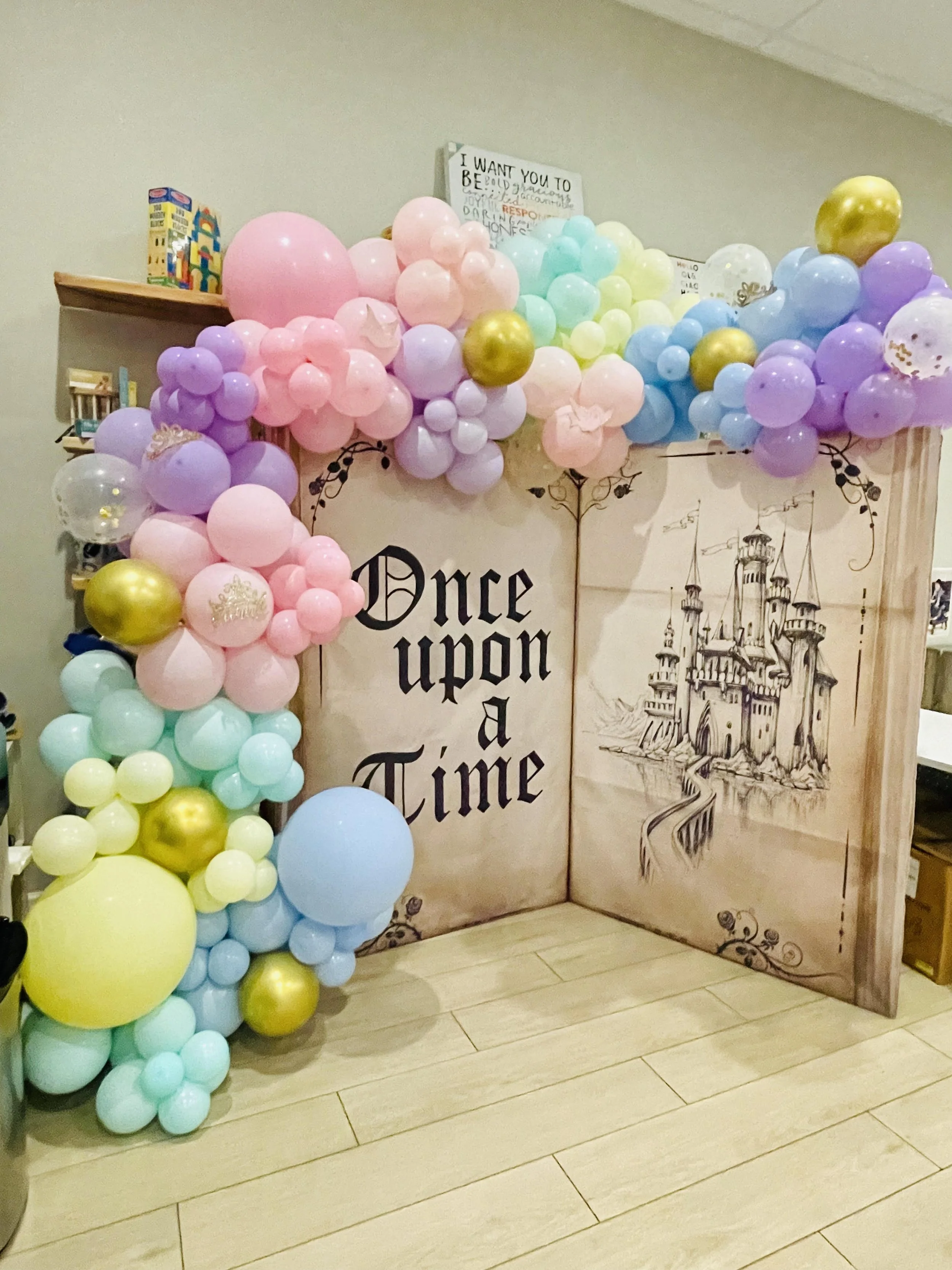 Balloon arch with pastel colors around a backdrop reading 'Once upon a time' and a drawing of a castle.