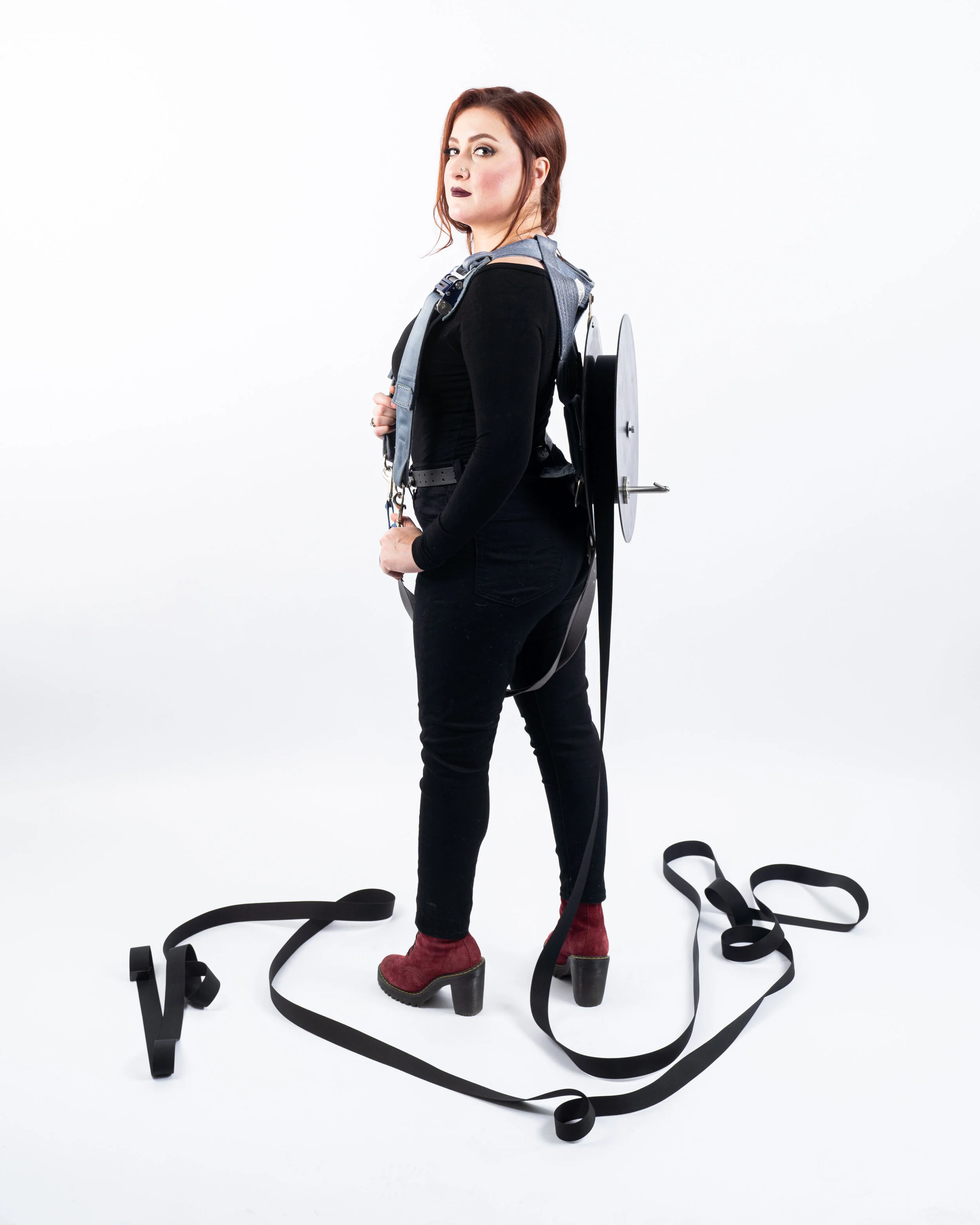 LISA_JETONNE-7.jpg Lisa Jetonne, Wearing the Wreckage 2021. Photo of a woman in black wearing a modified parachute harness disassembled and rearranged. Black webbing is unraveled on the ground at her feet.