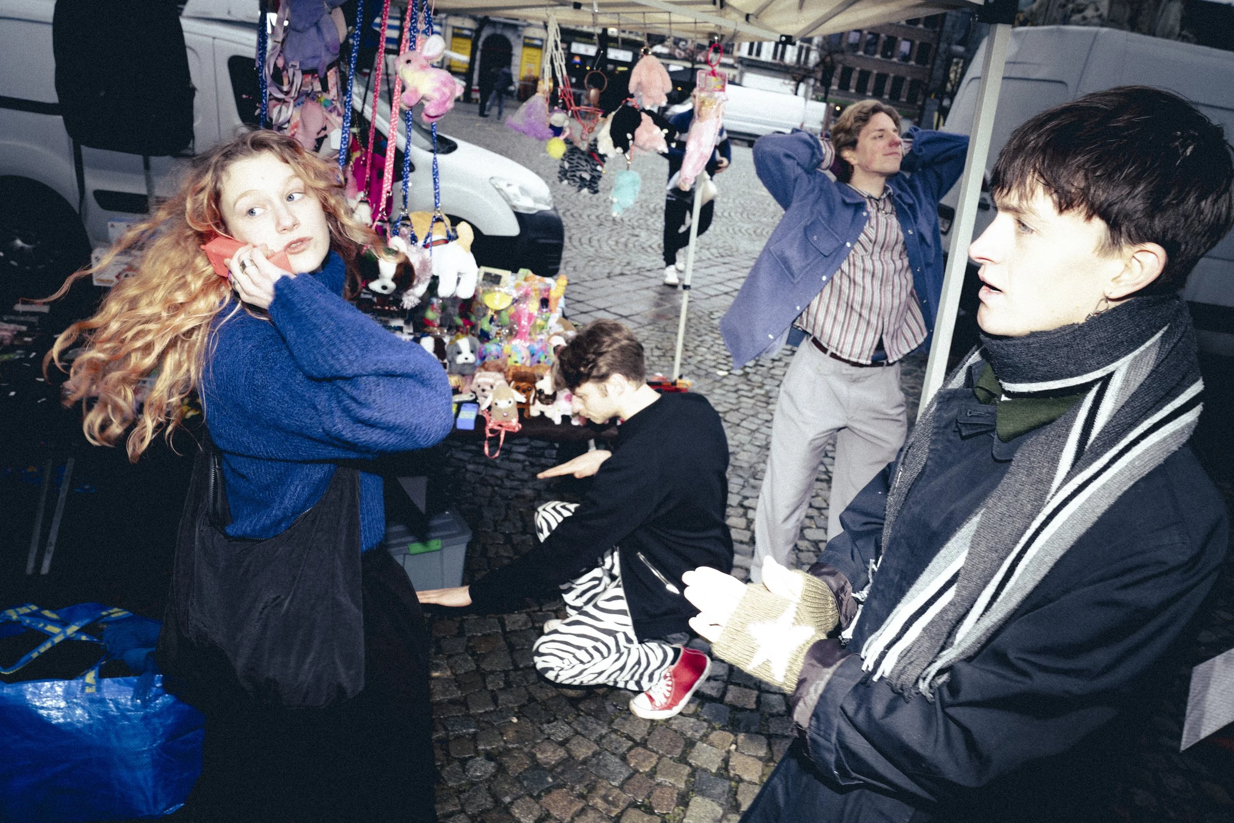 Mensen op een markt met speelgoed, waaronder knuffels en kleine dieren, en een vrouw die met een telefoon aan haar oor spreekt.