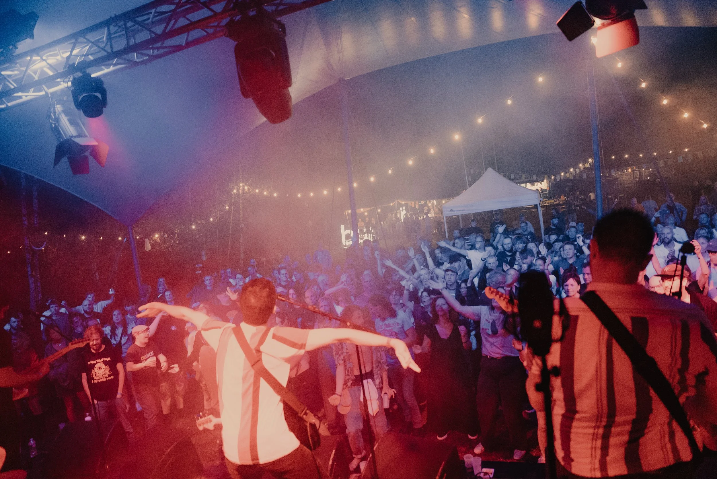 Een groep mensen bij een feest met muziek en verlichting, er wordt gedanst en genoten.