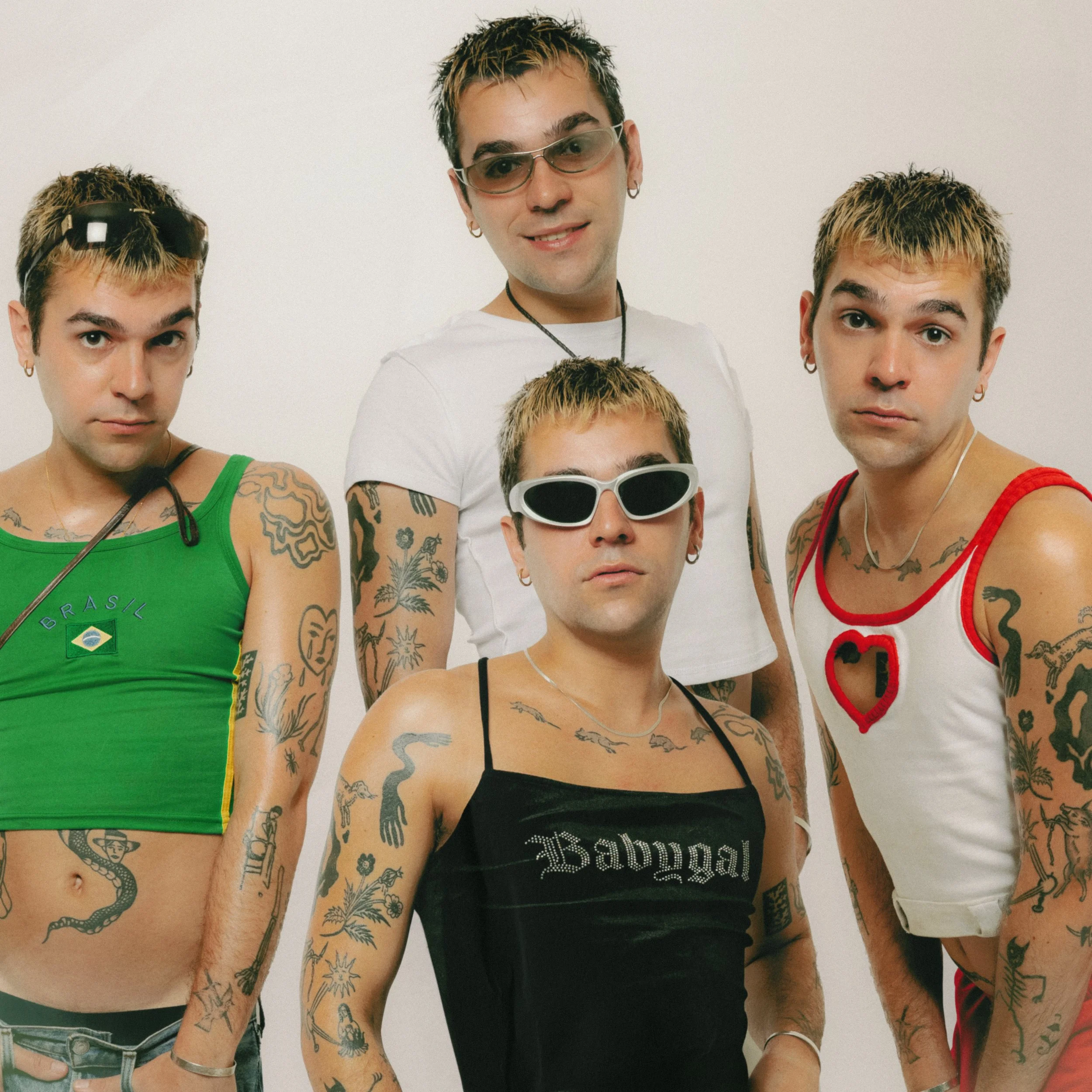 Vijf jonge mensen met tattoos en piercings, enkele dragen sportieve kleding en sieraden, allemaal staan voor een witte achtergrond.