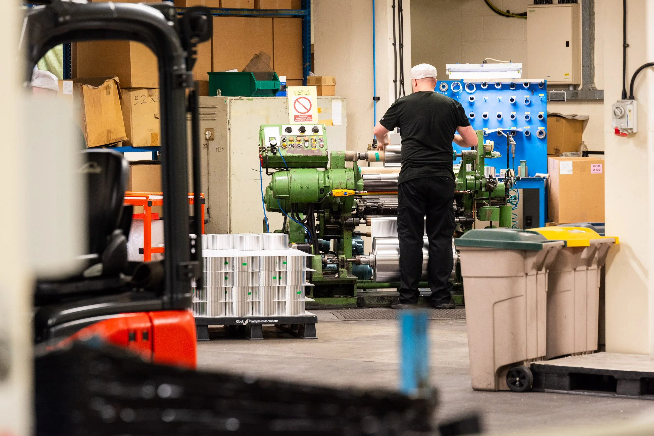 Factory worker operating green industrial foil machine in commercial production facility.