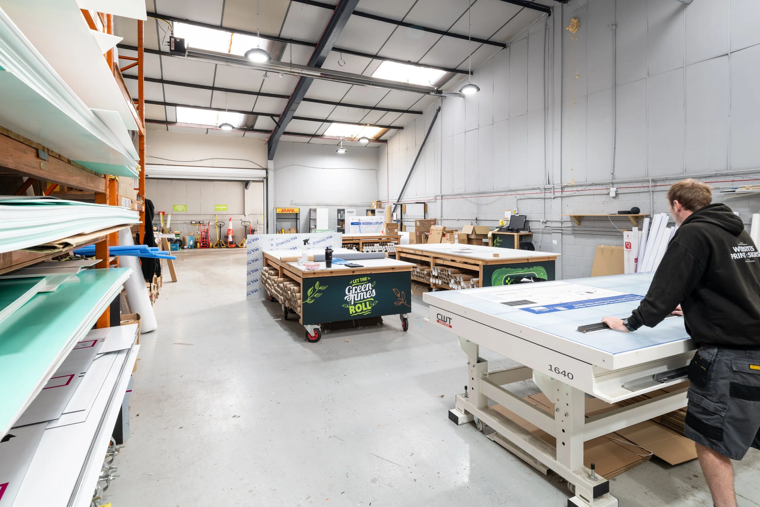 Wide view of large format printing and sign-making workshop with cutting tables and production equipment.