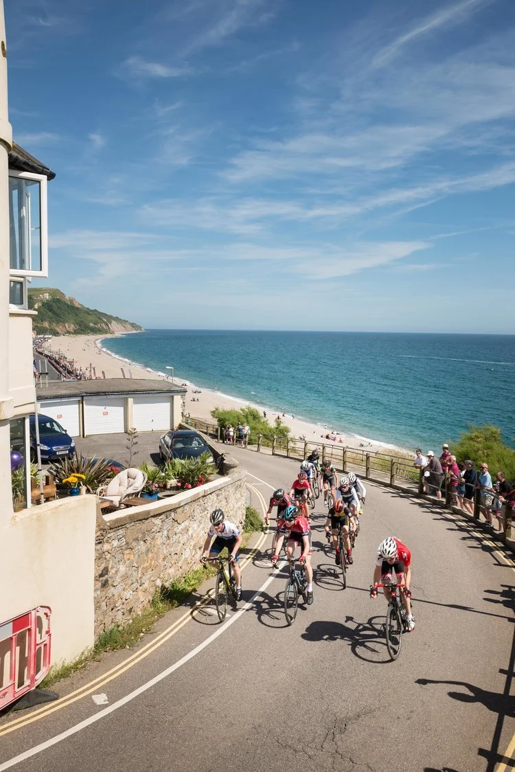 A beautiful photograph of cyclists racing around a corner on a road with the sea and sky in the background