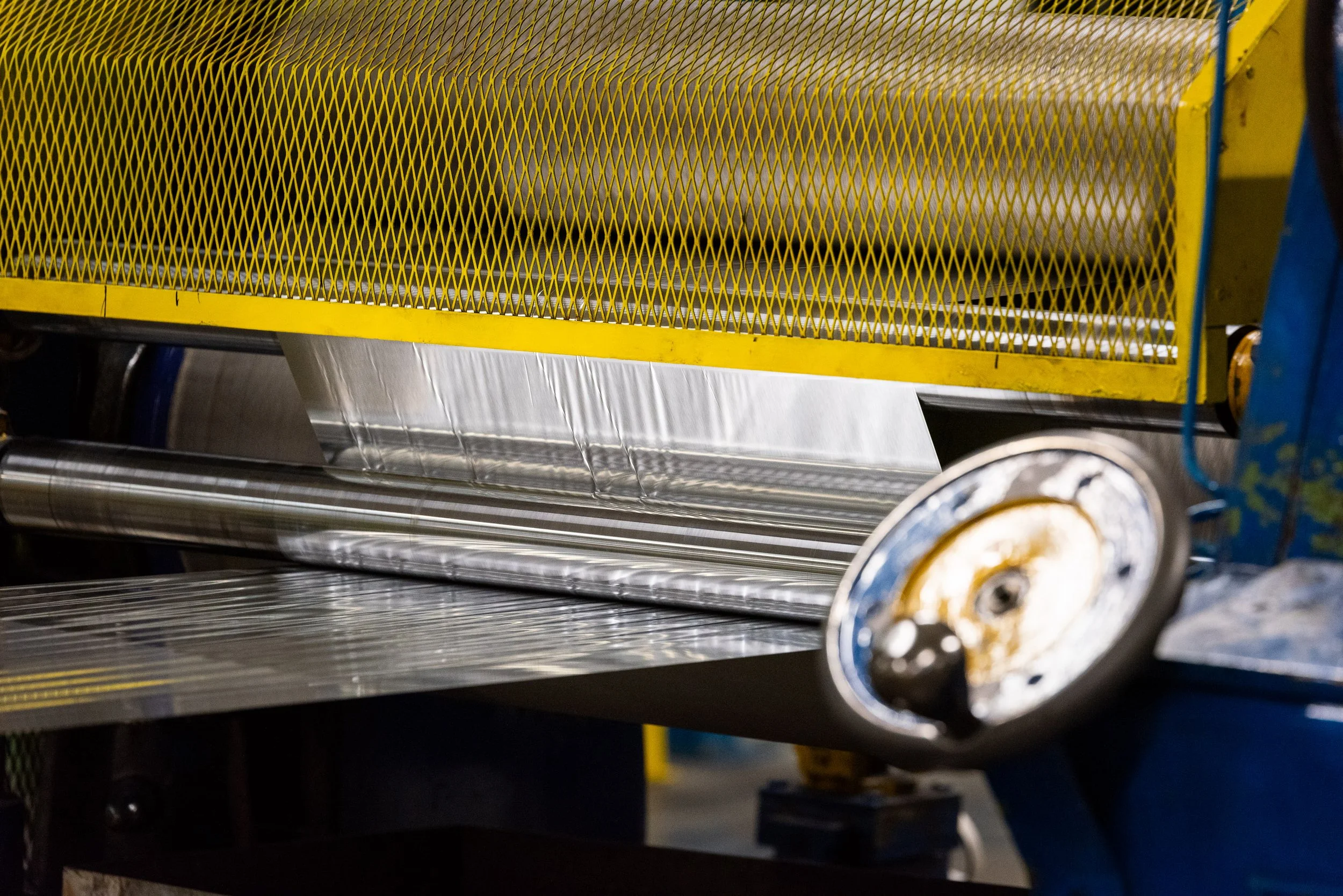 Industrial machine feeding aluminium foil sheet through rollers in a factory setting.
