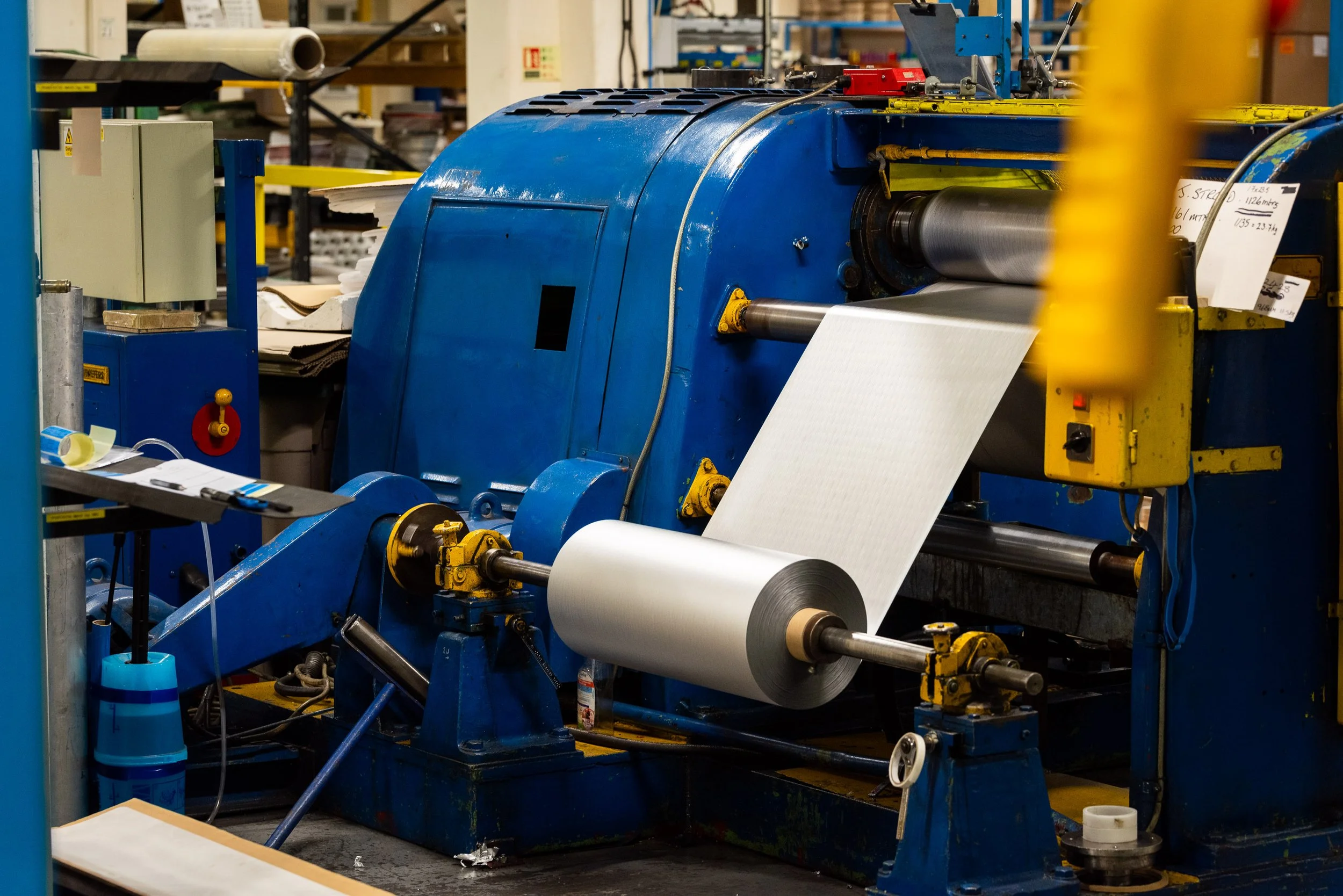 Industrial foil roll unwinding on heavy-duty machine in a commercial manufacturing workshop.