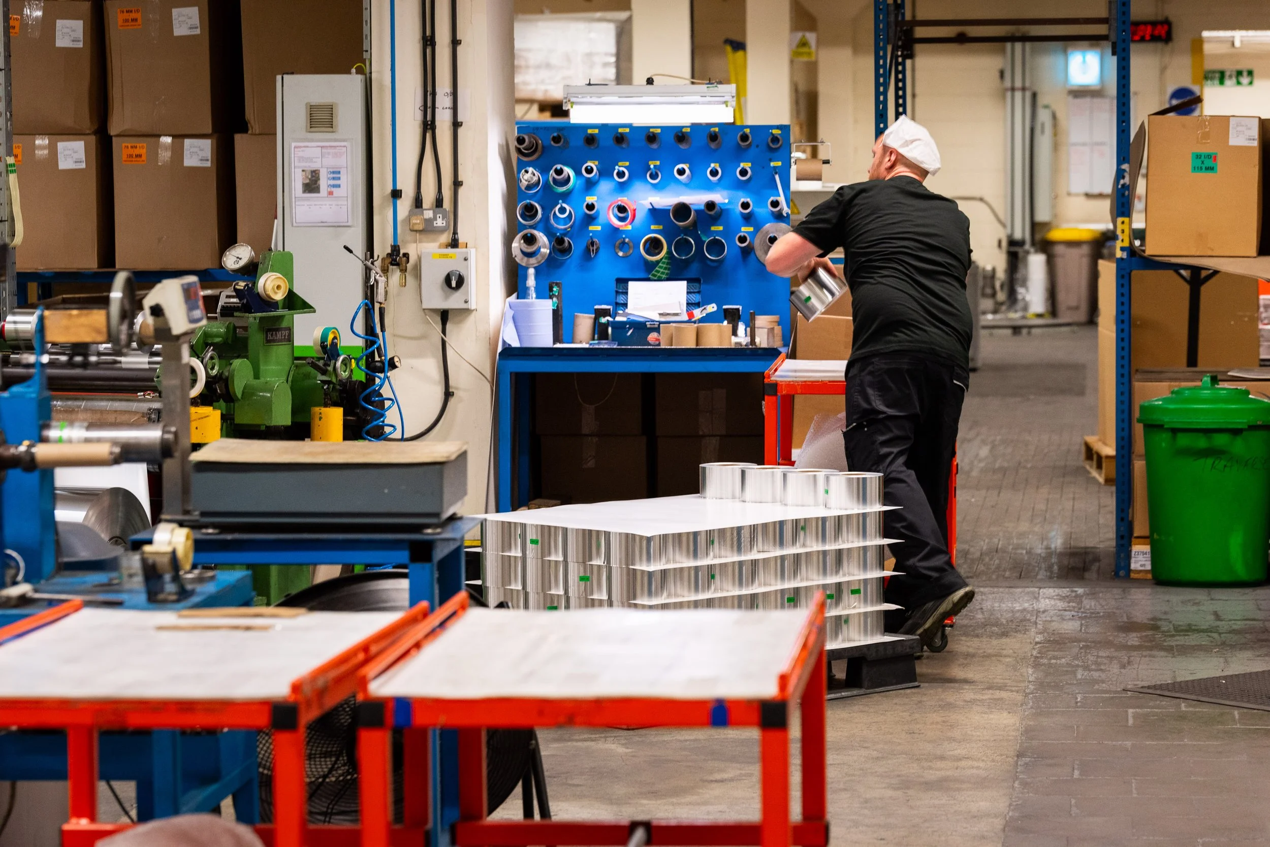 Factory worker handling processed aluminium foil rolls in an industrial workshop with heavy machinery.