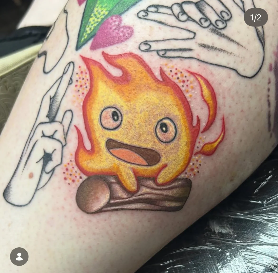 Tattoo of a cartoon flame with a cute face, sitting on a wooden log, surrounded by black-and-white outlined hands making peace signs, and a pink heart and green shape in the background. studio ghibli. 
