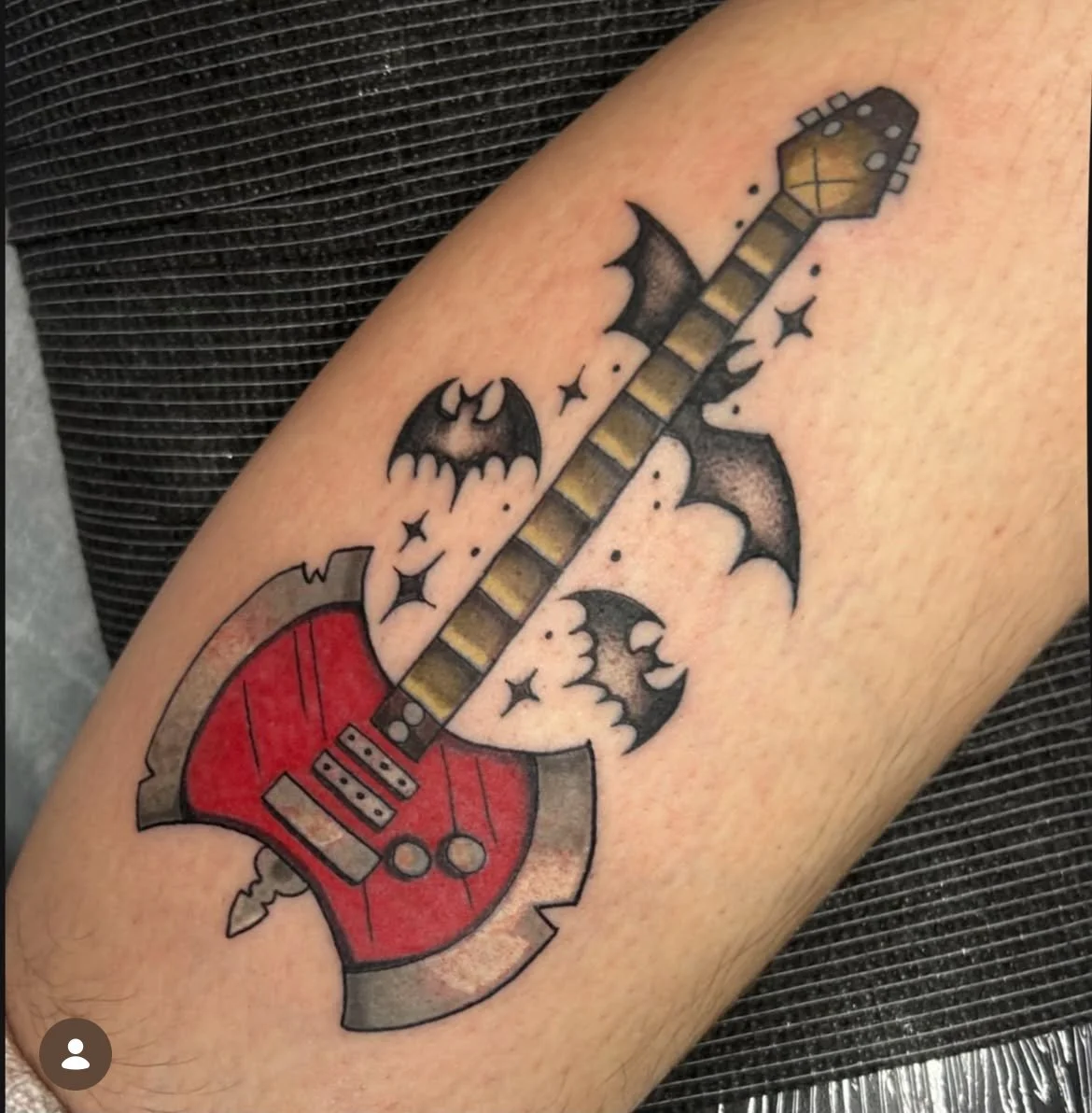 Tattoo of a red electric guitar surrounded by bats and stars.