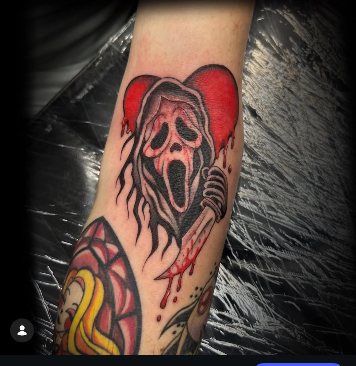 Tattoo of the Ghostface scream mask with dripping blood and a microphone on the arm.