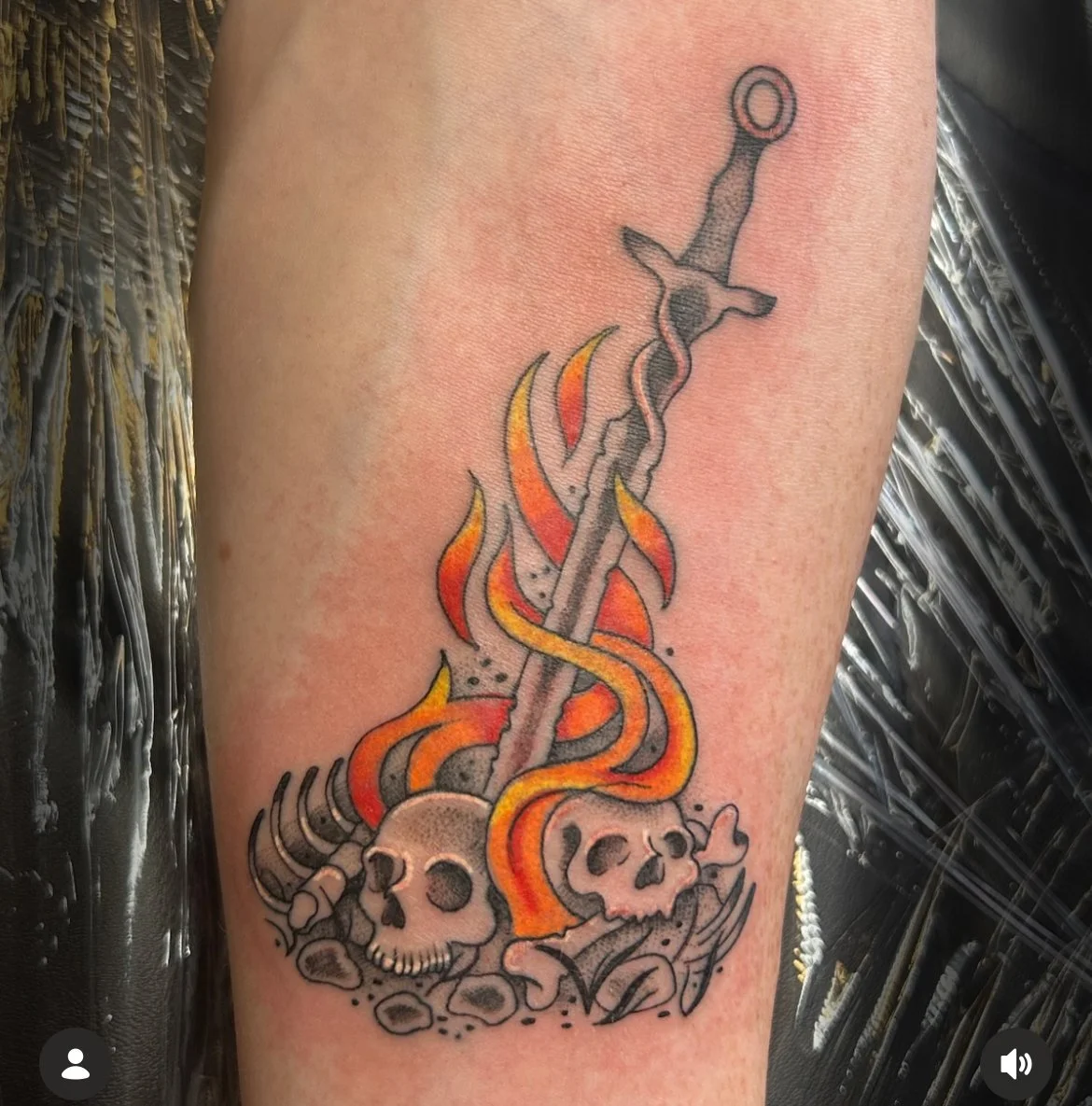 Tattoo featuring a sword with flames and two skulls at the base.