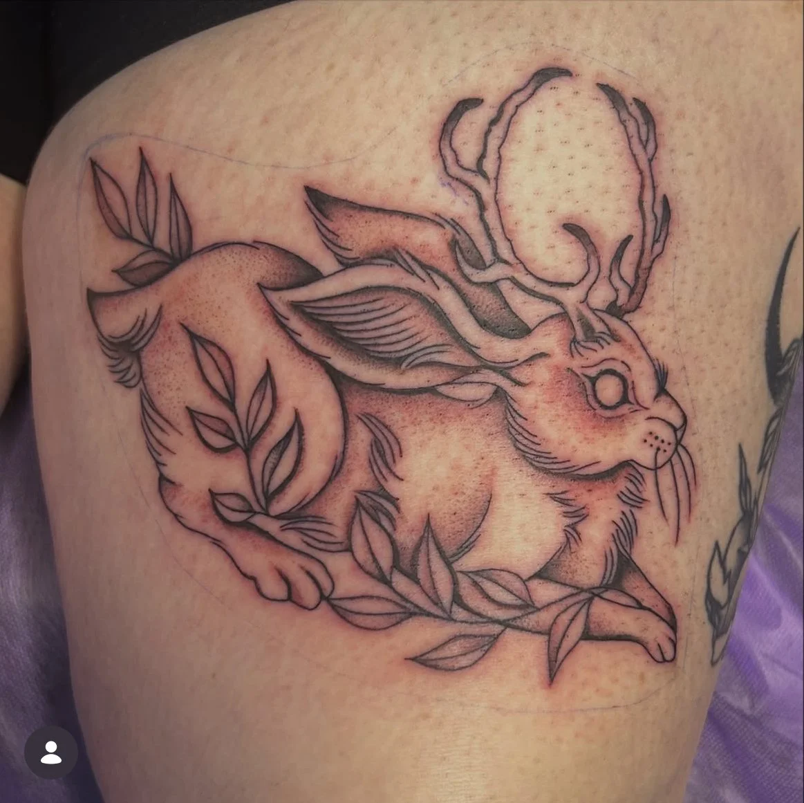 Tattoo of a rabbit with antlers, leaves, and a circular moon or sun in the background. jackalope
