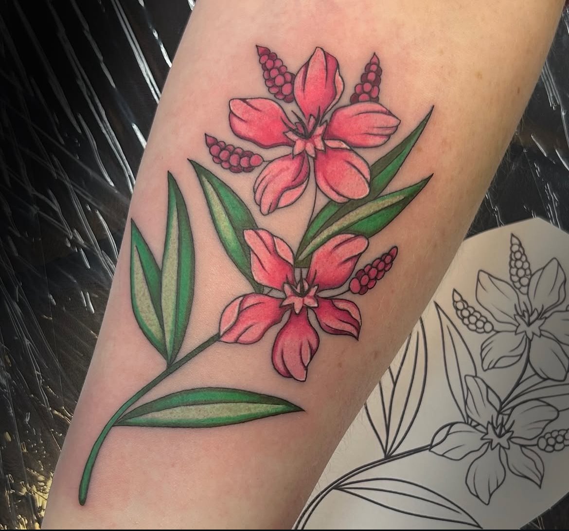Colored tattoo of pink and orange lilies with green leaves on a person's arm, with a black outline sketch of the design nearby.