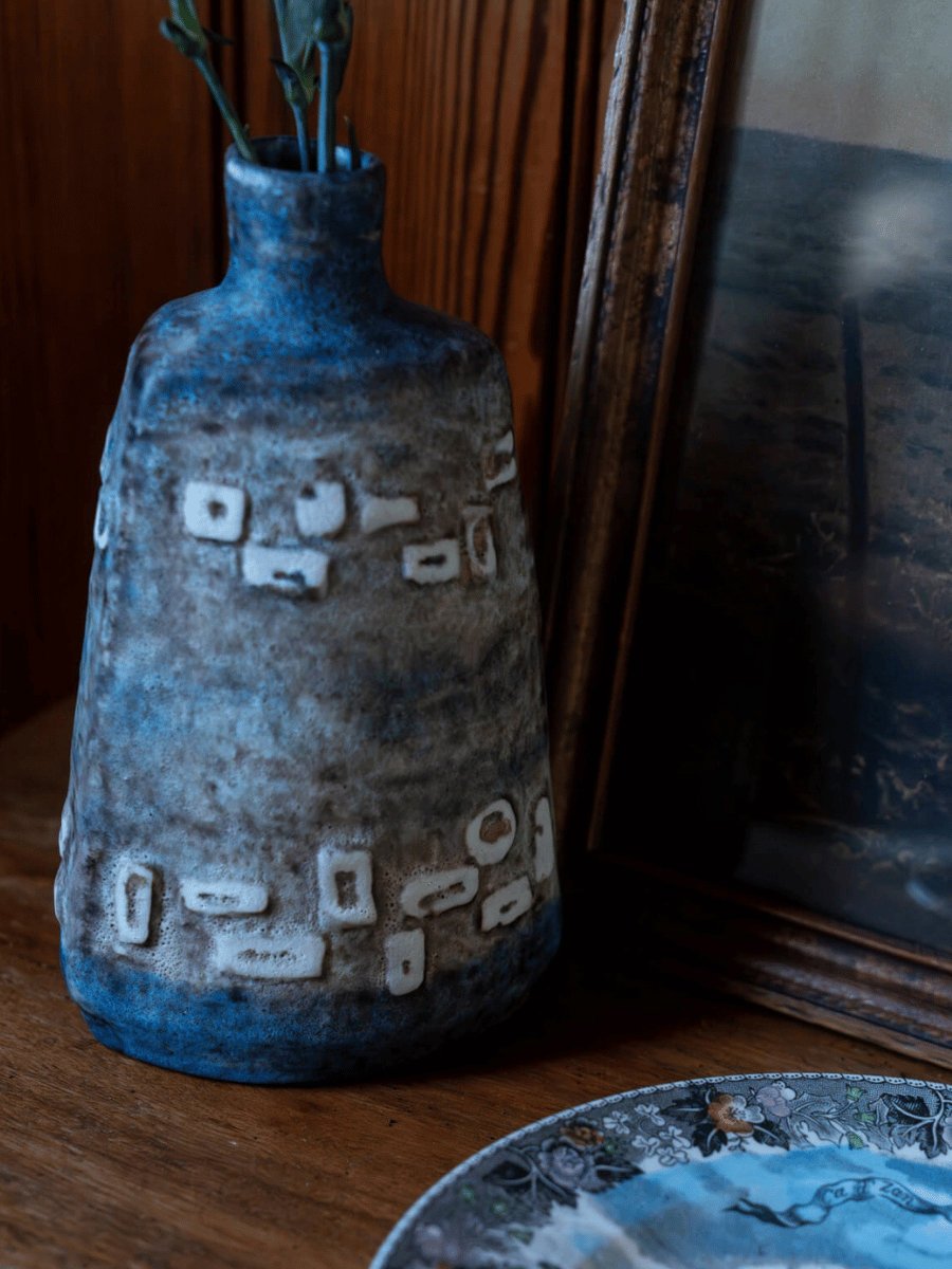 Blue-gray stoneware bottle vase with a narrow neck, round shoulders, mottled glaze and raised white geometric marks.