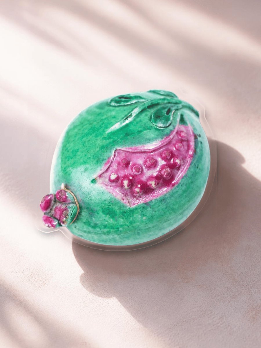Miniature green porcelain pomegranate opened to reveal raised raspberry-pink seeds.