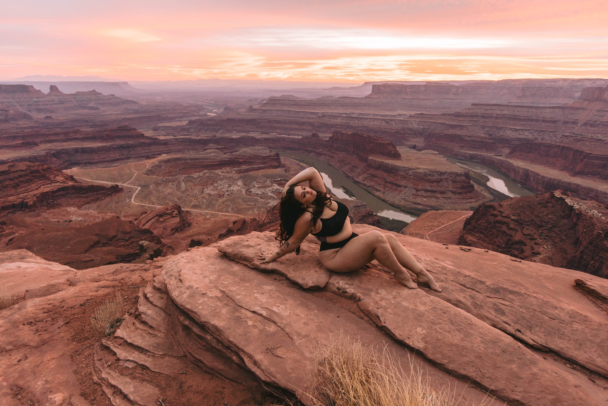 A woman in black clothing sitting on red rock at the Grand Canyon during sunset.